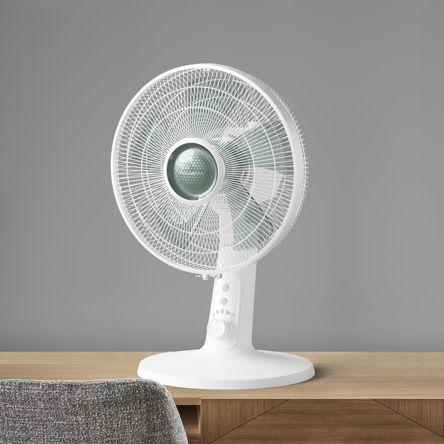 White fan on a wooden table, gray wall in the background.