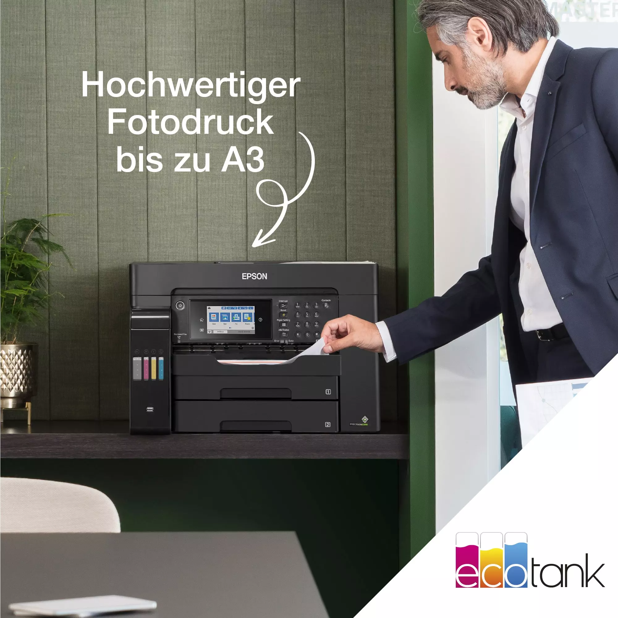 Ein Mann legt Papier in einen Drucker ein. Der Drucker steht auf einem Schreibtisch vor einer grünen Wand.