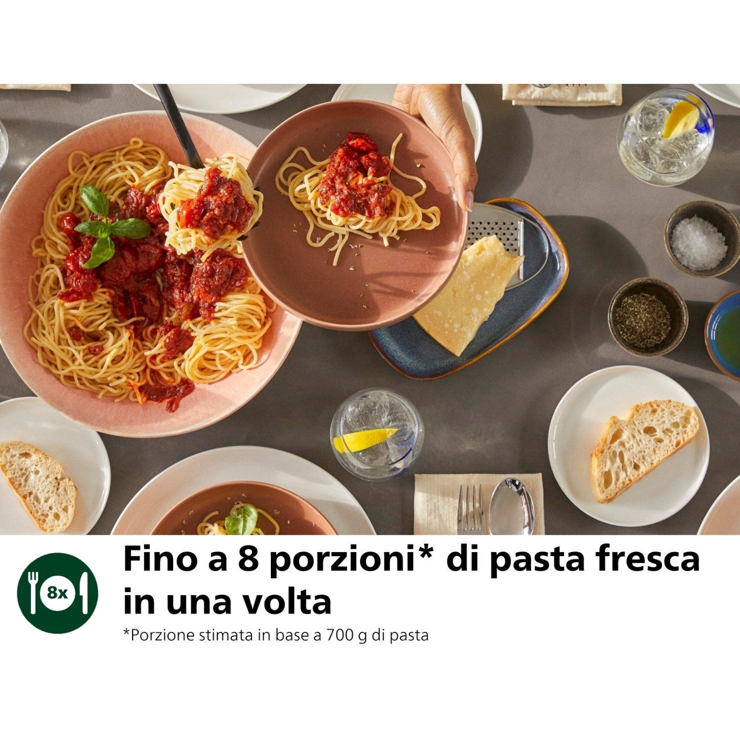 Tavolo con spaghetti in una ciotola, parmigiano e altri alimenti. Una mano sta servendo.