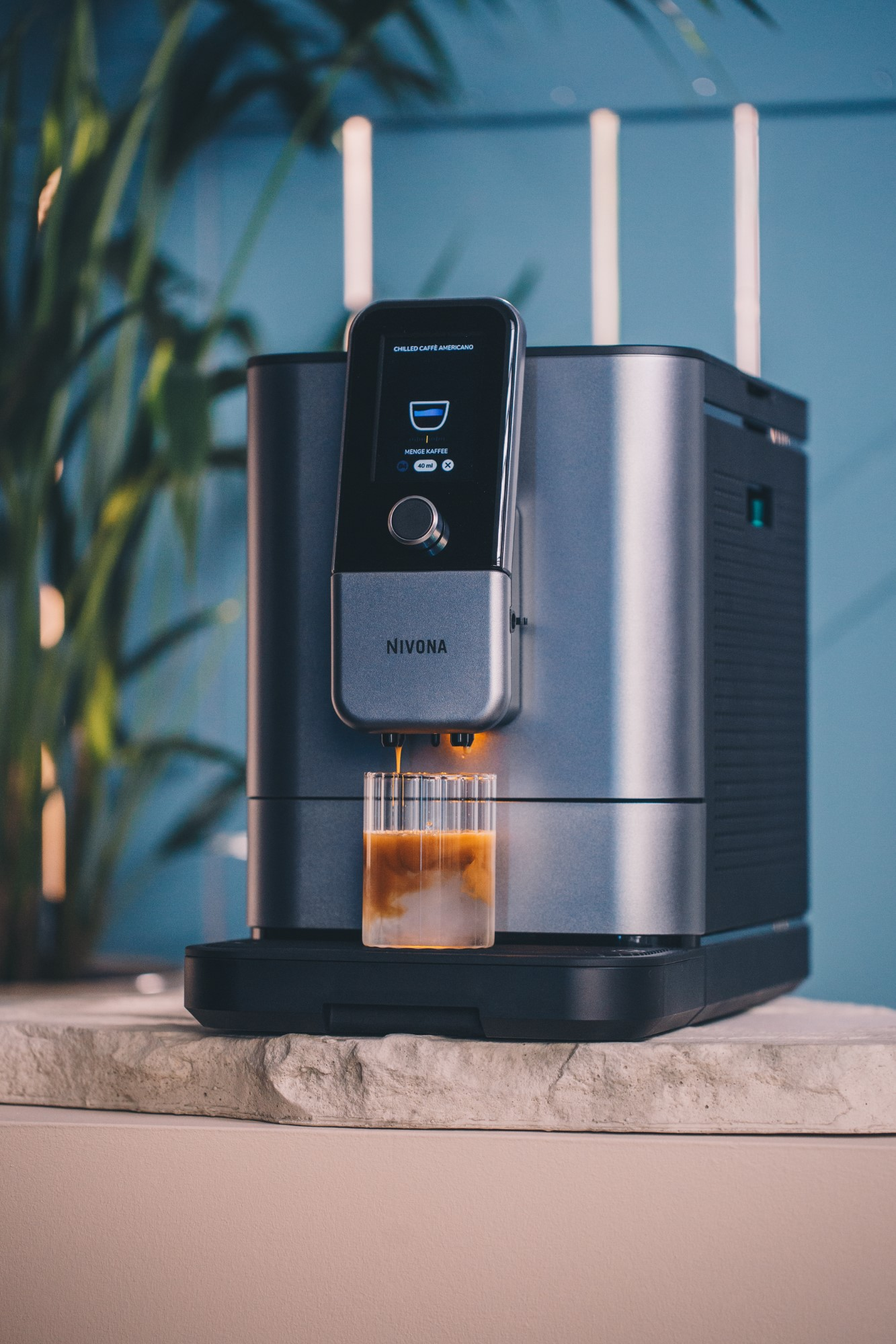 Srebrno-czarny ekspres do kawy ze szklanką kawy, na kamiennej powierzchni.