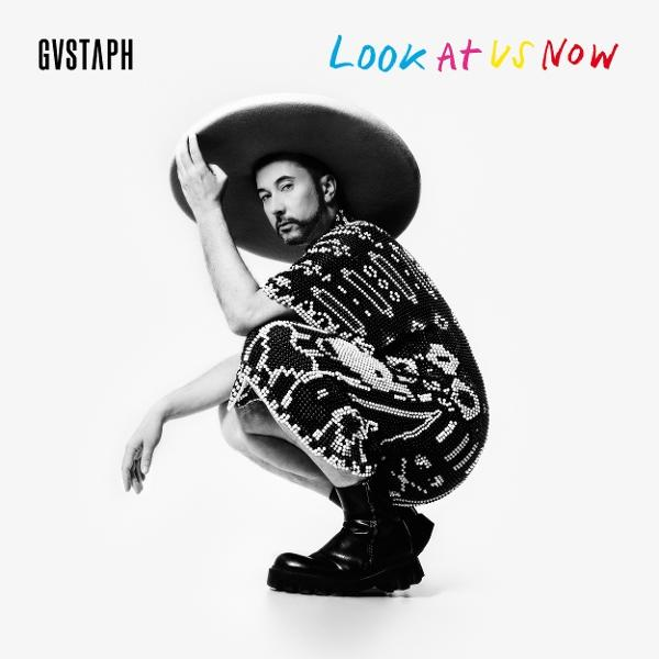 Homme avec un chapeau et une chemise à motifs, accroupi. Texte 'LOOK AT US NOW' et 'GVSTAPH'.