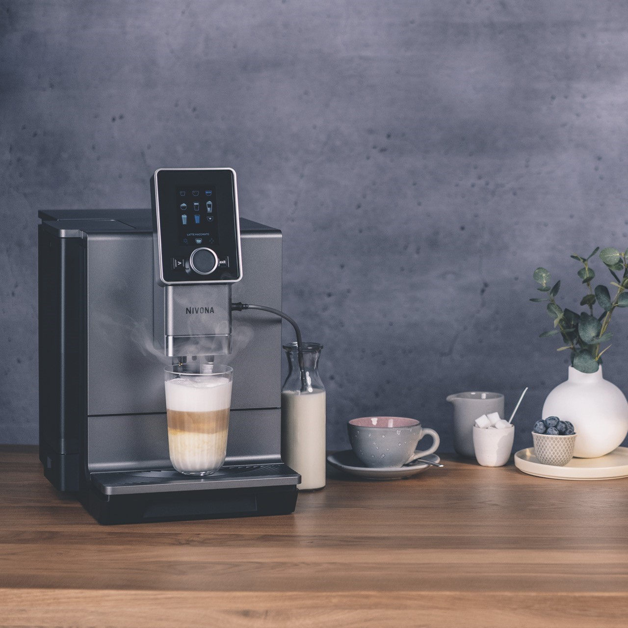 Ekspres do kawy dozujący kawę do szklanki. Butelka mleka i inne przedmioty obok.