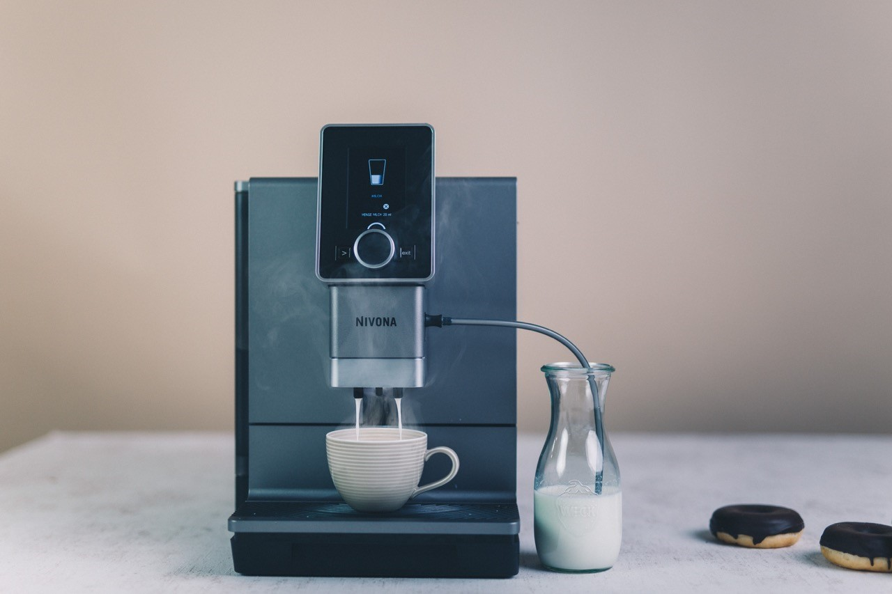 Ekspres do kawy dozujący kawę do filiżanki. W widoku znajduje się również pojemnik na mleko i pączki.