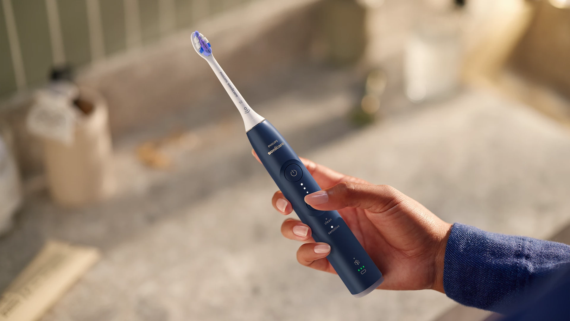 Person hält eine blau-weiße elektrische Zahnbürste. Die Zahnbürste hat Knöpfe und einen Kopf.