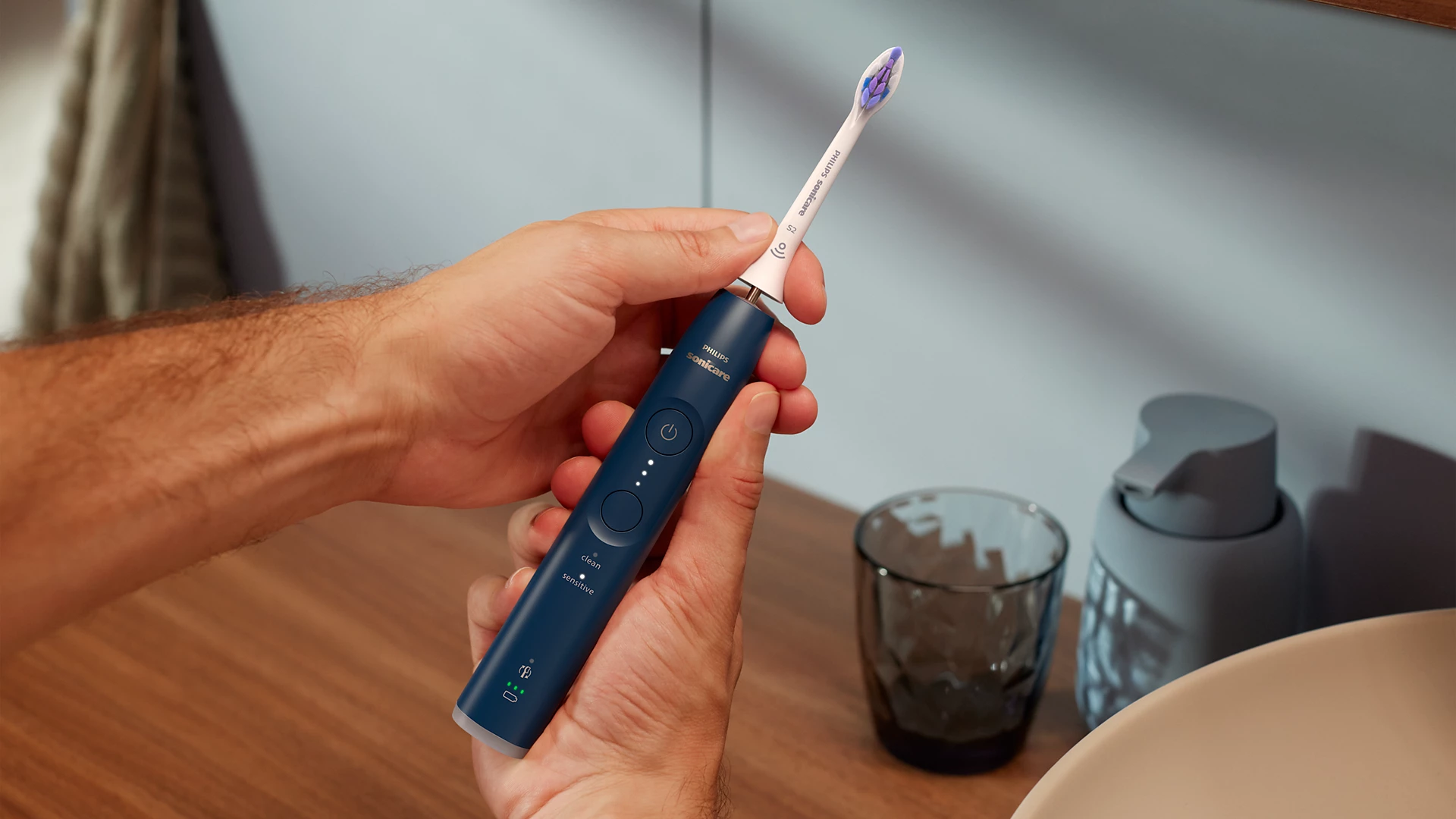 Person hält blaue und weiße Zahnbürste. Badezimmer-Theke und Waschbecken im Hintergrund.