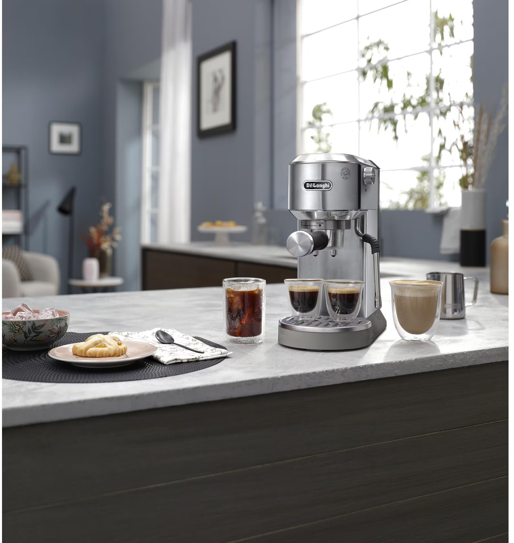 Bancone con macchina per espresso, bicchieri di caffè e cibo. Una finestra e l'arredamento della cucina sullo sfondo.