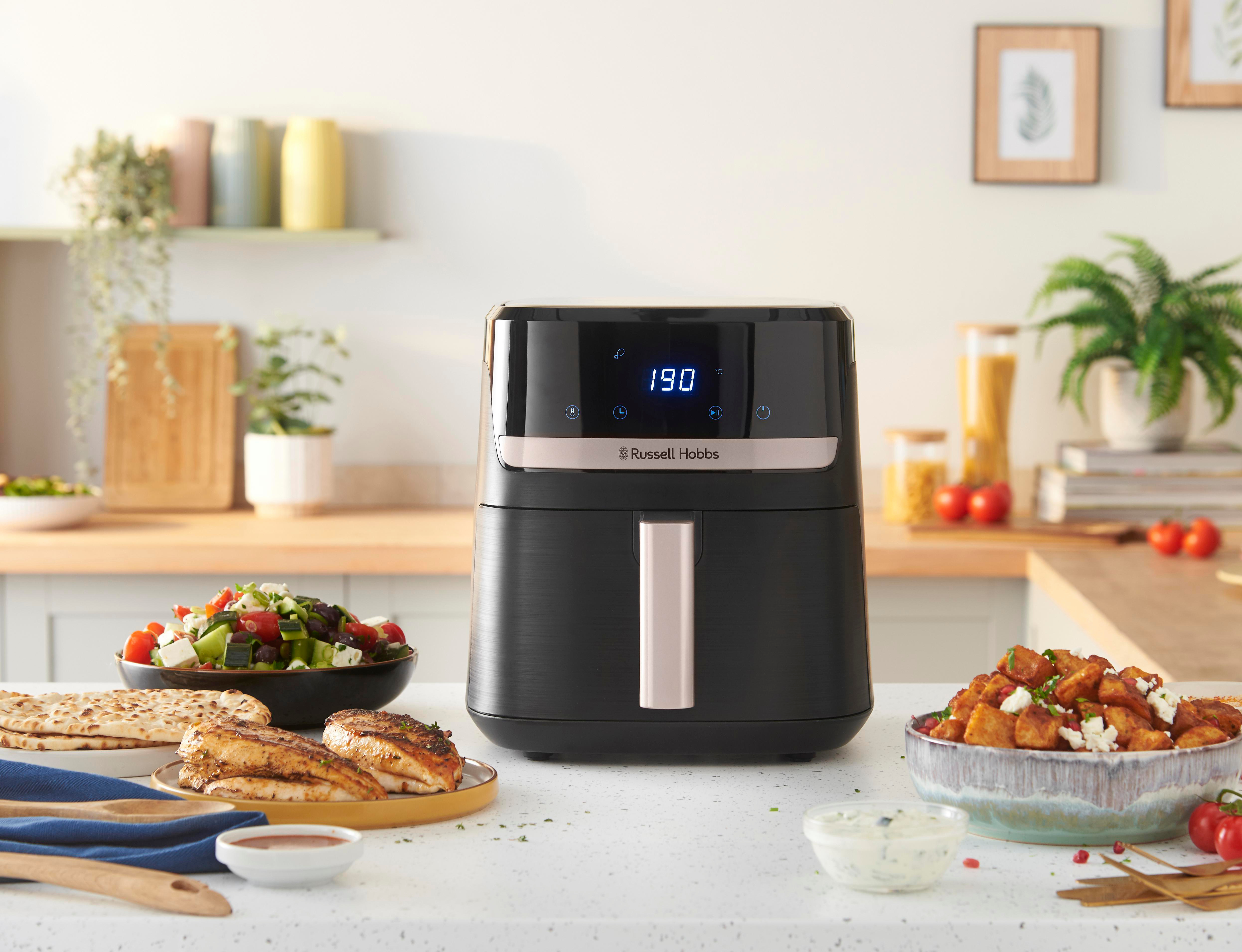 Schwarze Heißluftfritteuse mit Digitalanzeige auf der Küchentheke, umgeben von Essen.