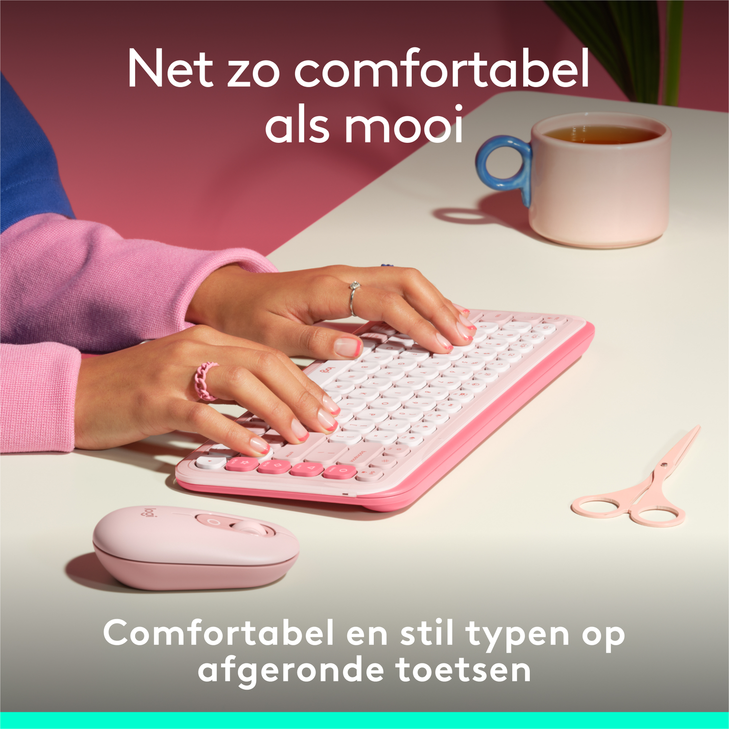 Handen die typen op een roze toetsenbord naast een muis, schaar en kopje thee.