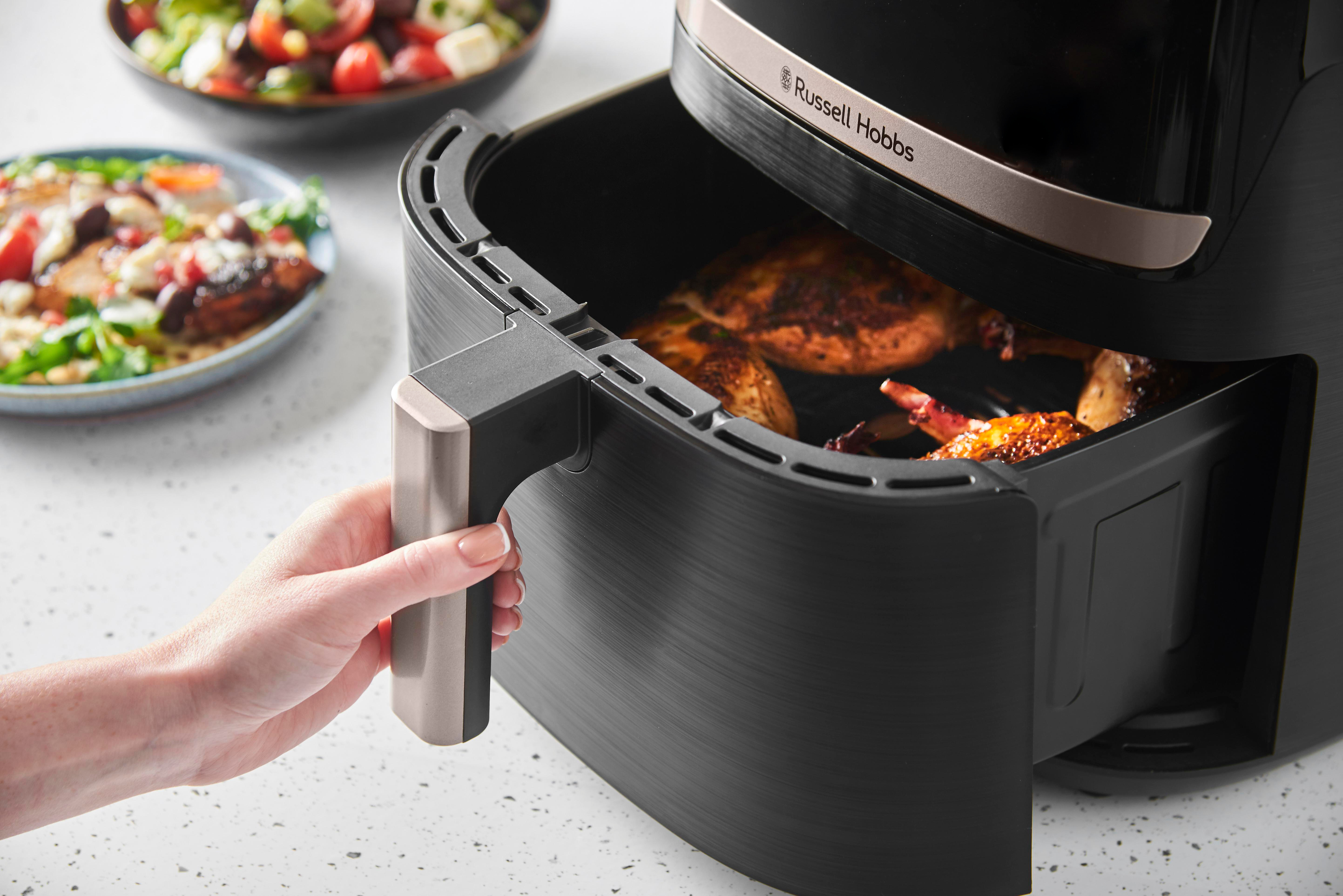 Hand einer Frau hält einen Airfryer-Griff. Essen ist im Inneren des Frittierers.