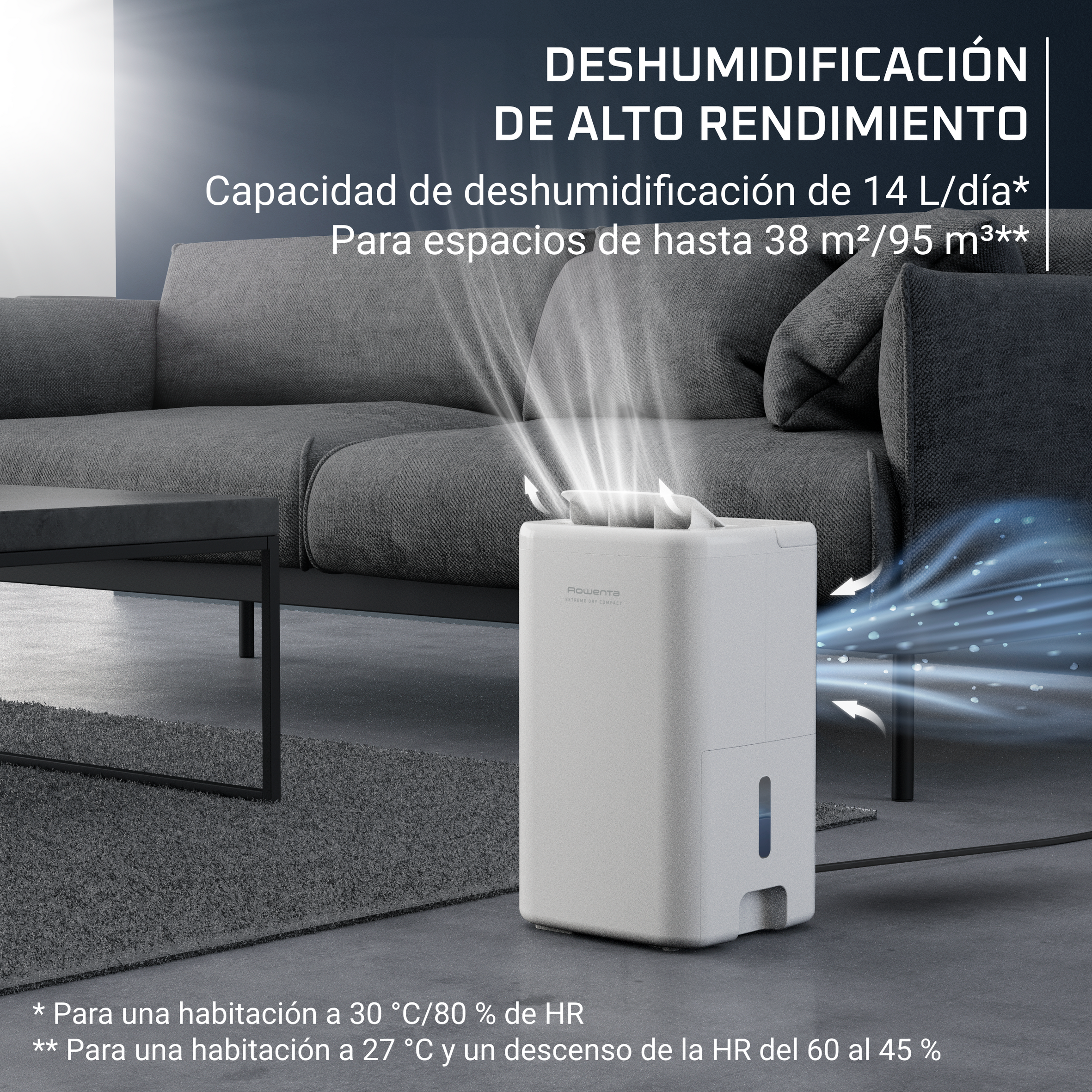 Un deshumidificador blanco en una sala de estar. La máquina está encendida, emitiendo vapor. Un sofá y una mesa grises están en el fondo.