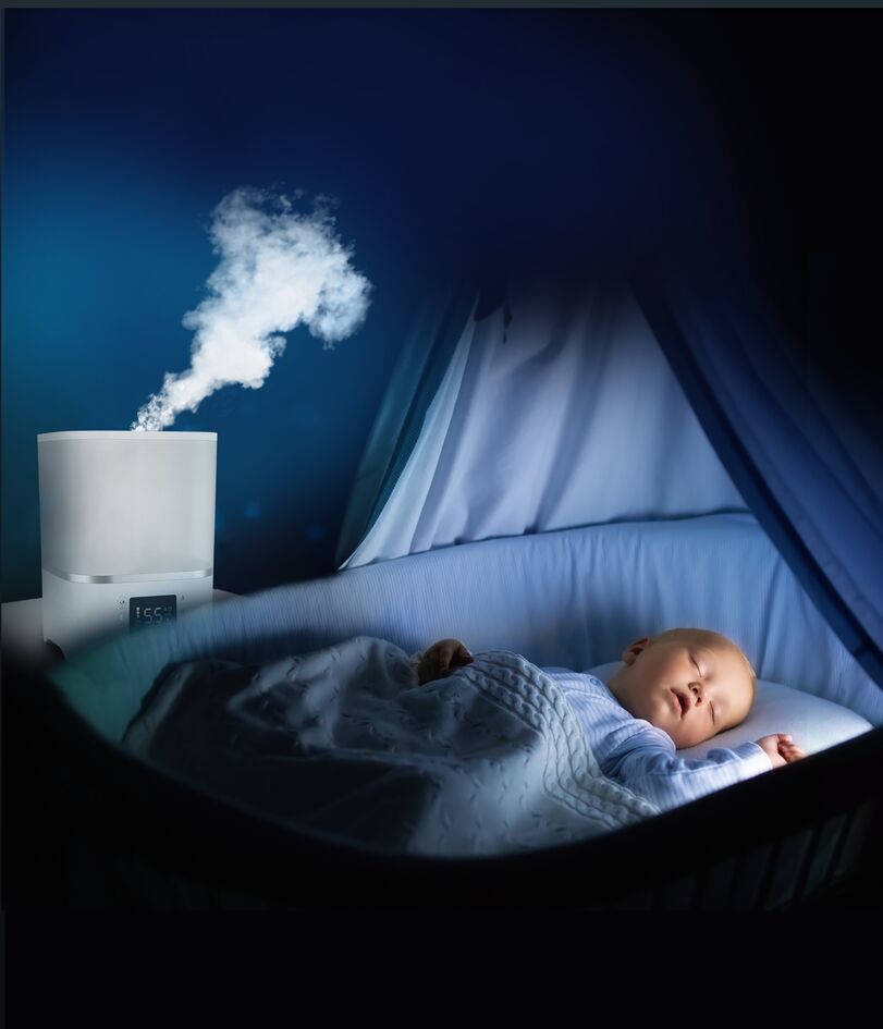 Un bebé duerme plácidamente en una cuna con un humidificador cerca.