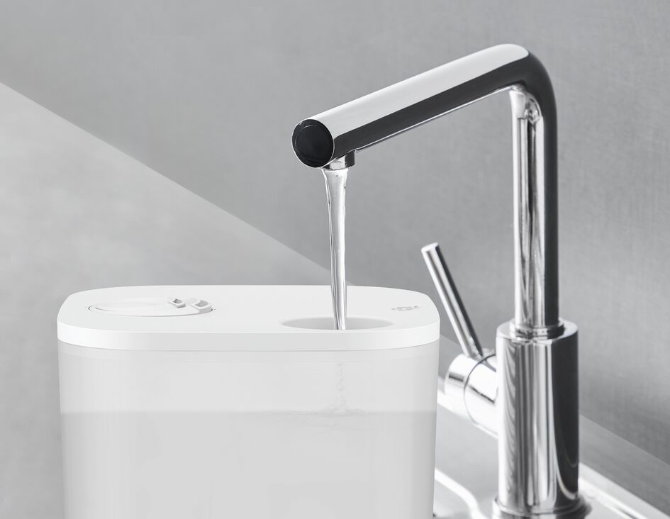 Un grifo de cocina con un chorro de agua que fluye hacia un recipiente blanco. El fondo es gris.