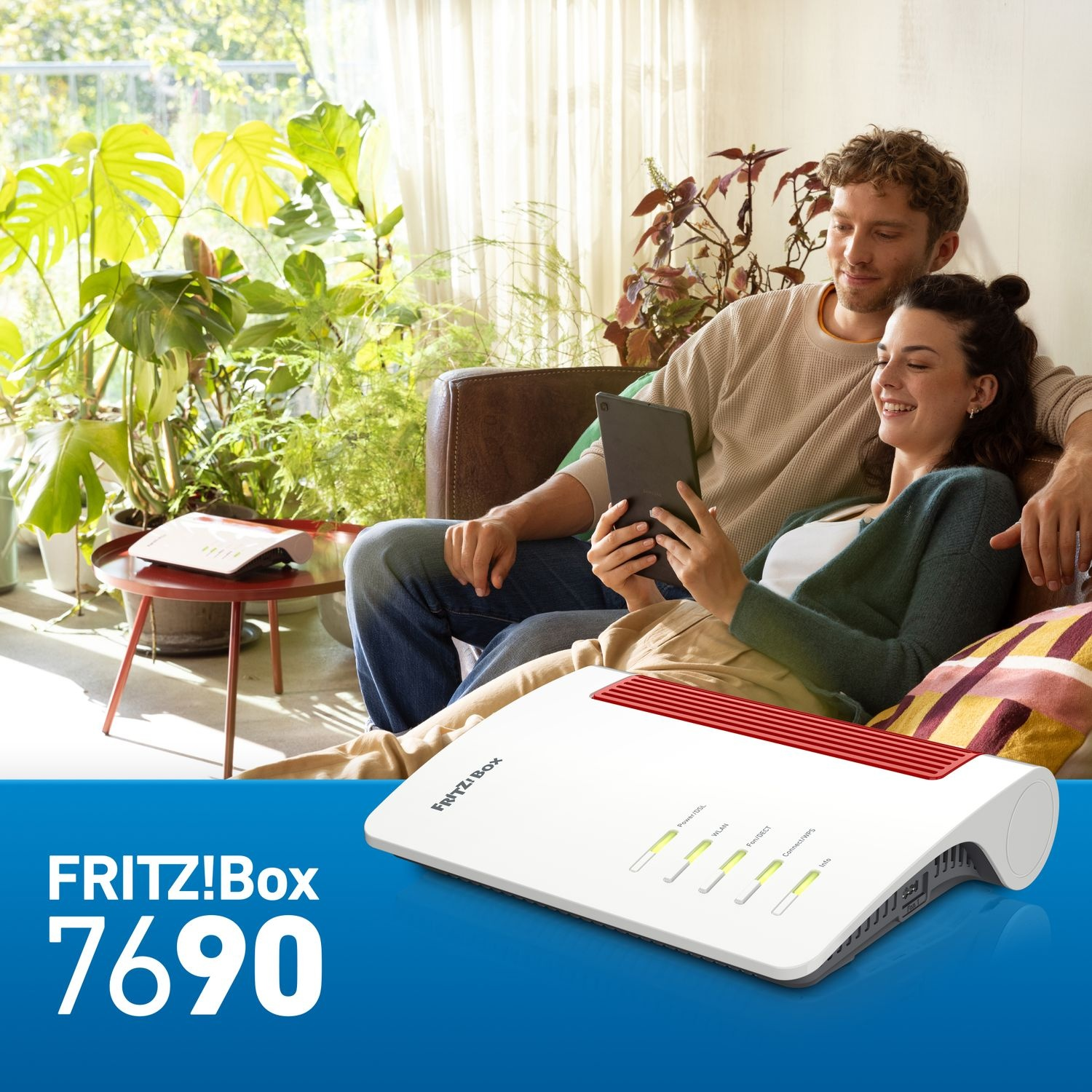 Een stel op een bank met een tablet, met een wit-roode FRITZ!Box 7690 router op de voorgrond.