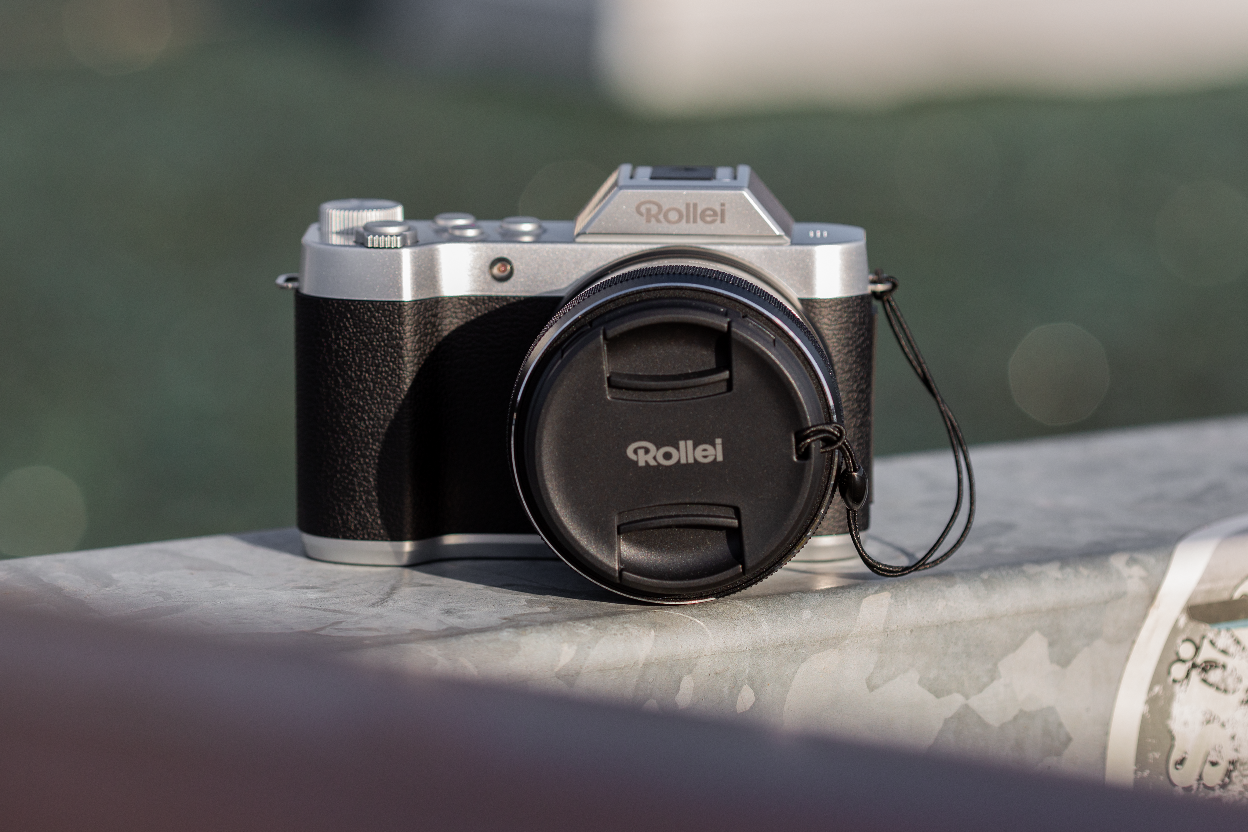 Fotocamera Rollei argento e nera con tappo dell'obiettivo su metallo, sfondo verde sfocato.