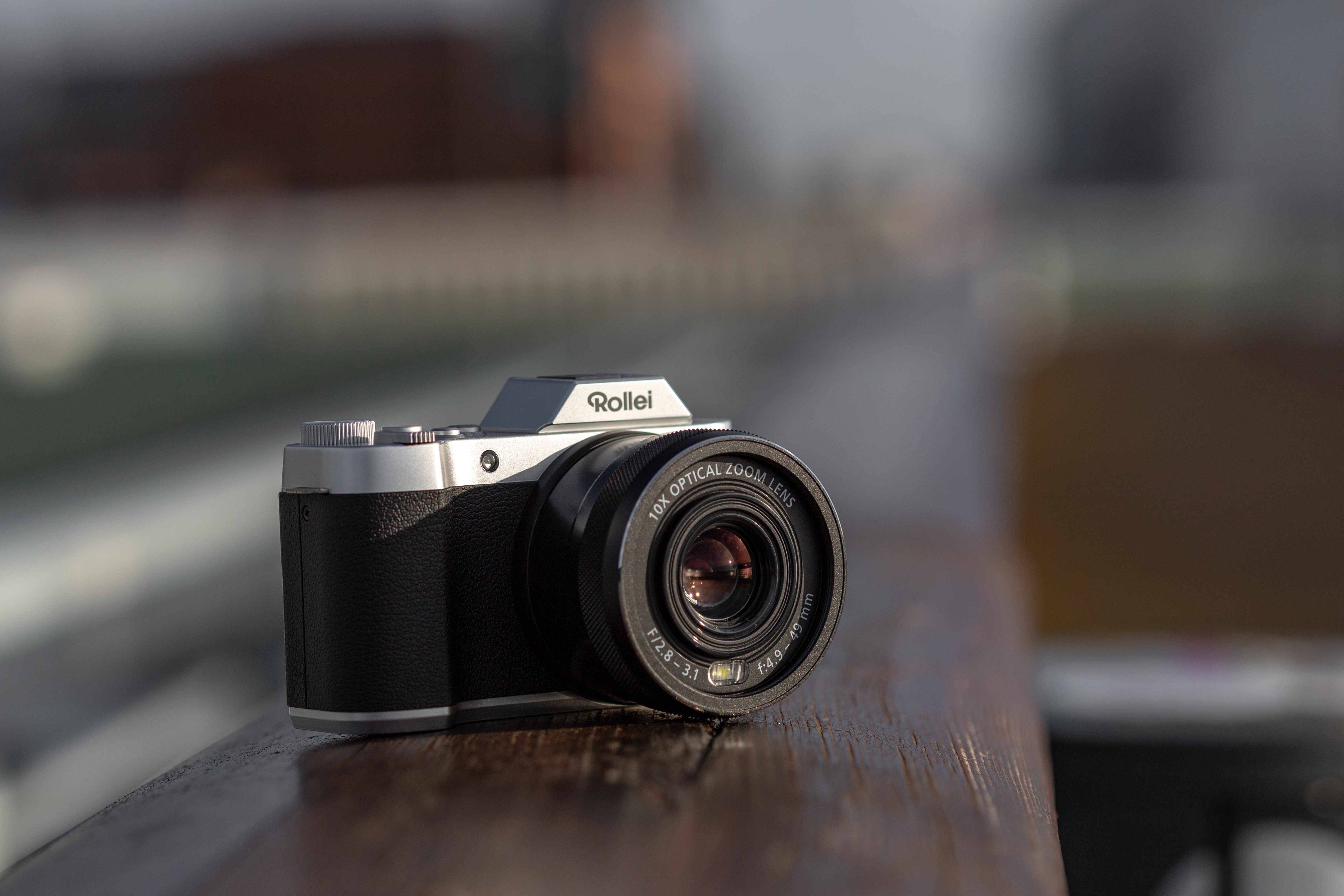Fotocamera Rollei argento e nera su una ringhiera di legno, con sfondo sfocato.
