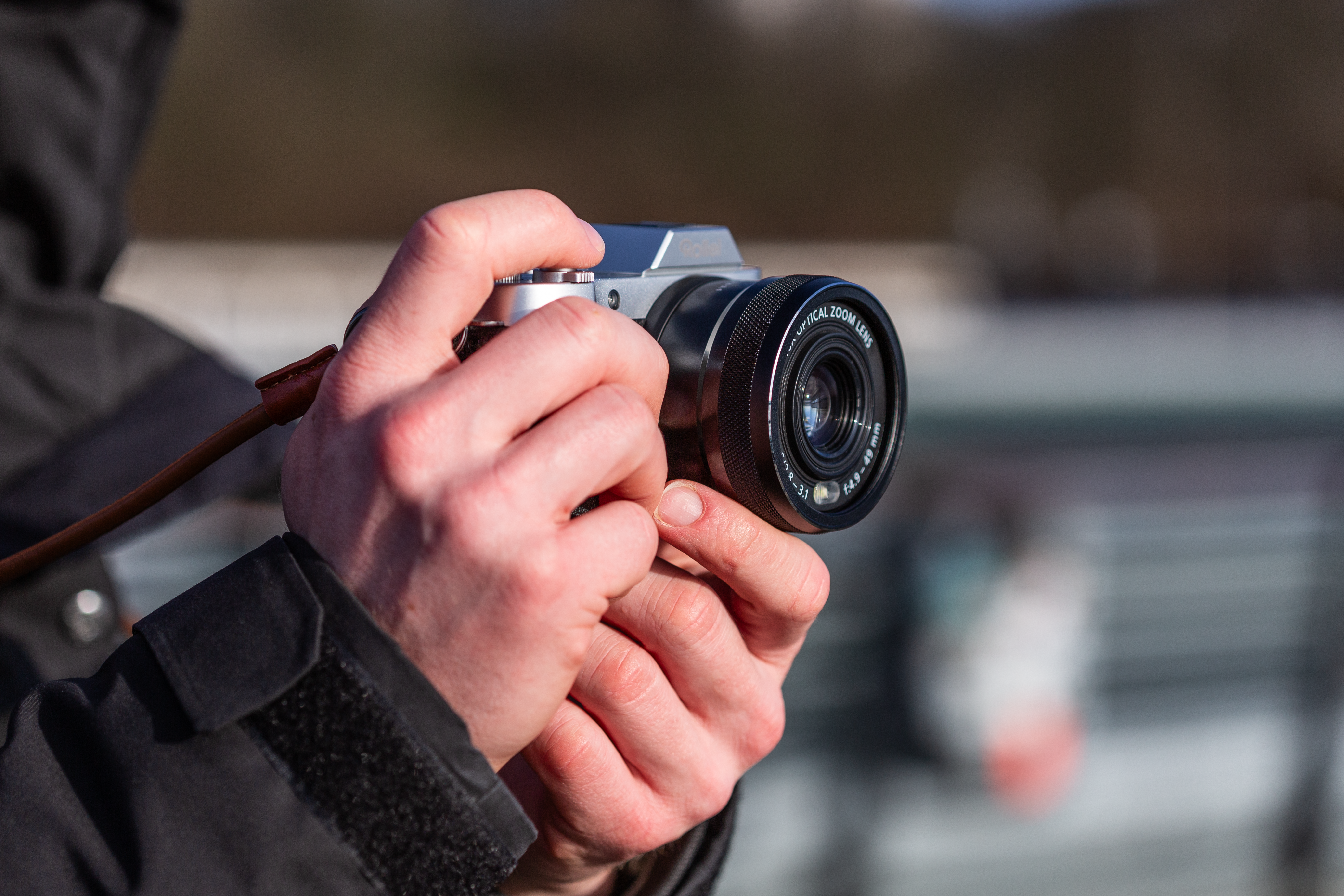 Una persona che tiene in mano una fotocamera argentata, focalizzata sull'obiettivo.