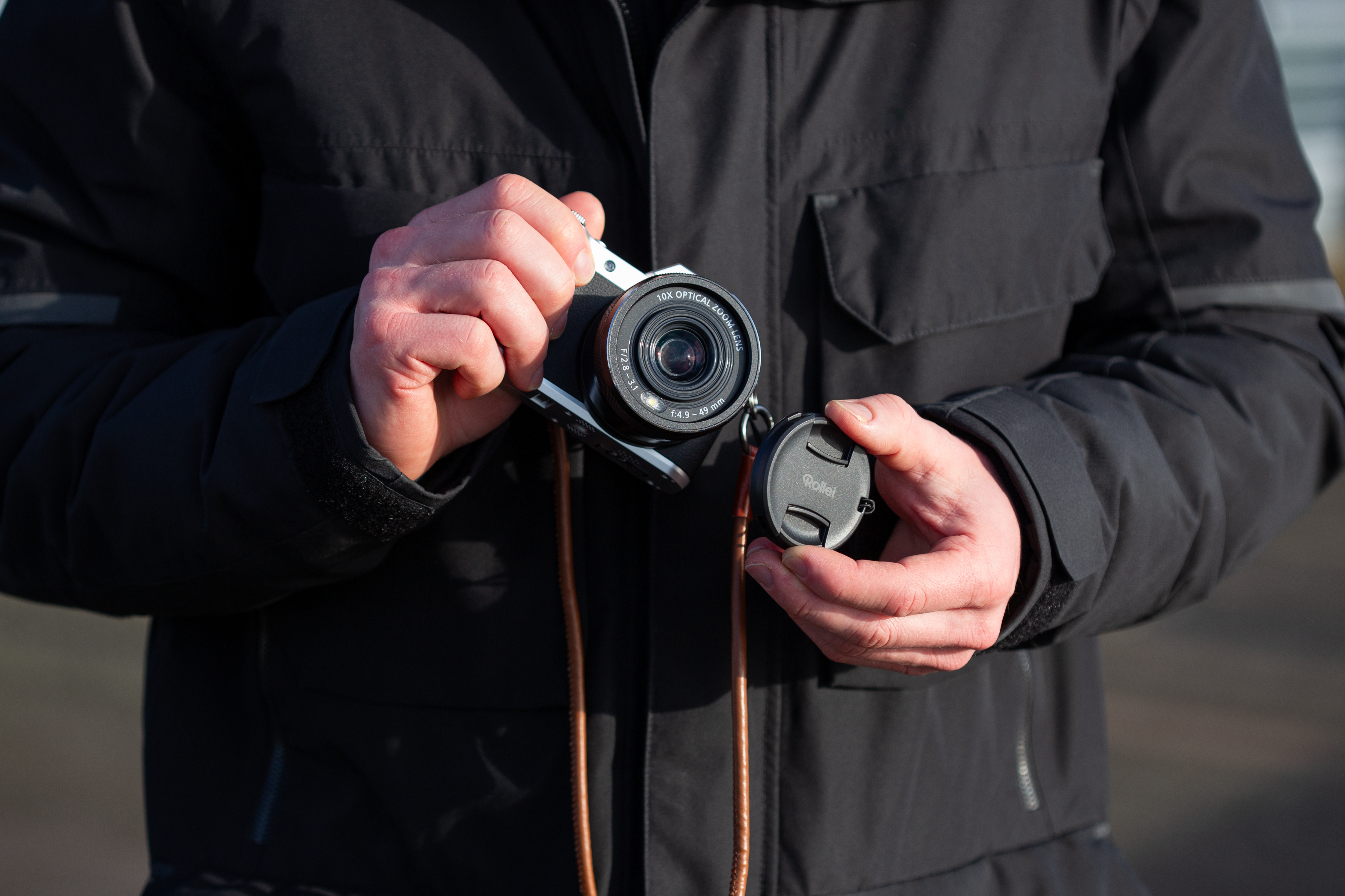 Persona in giacca nera tiene una macchina fotografica argento con tappo nero.
