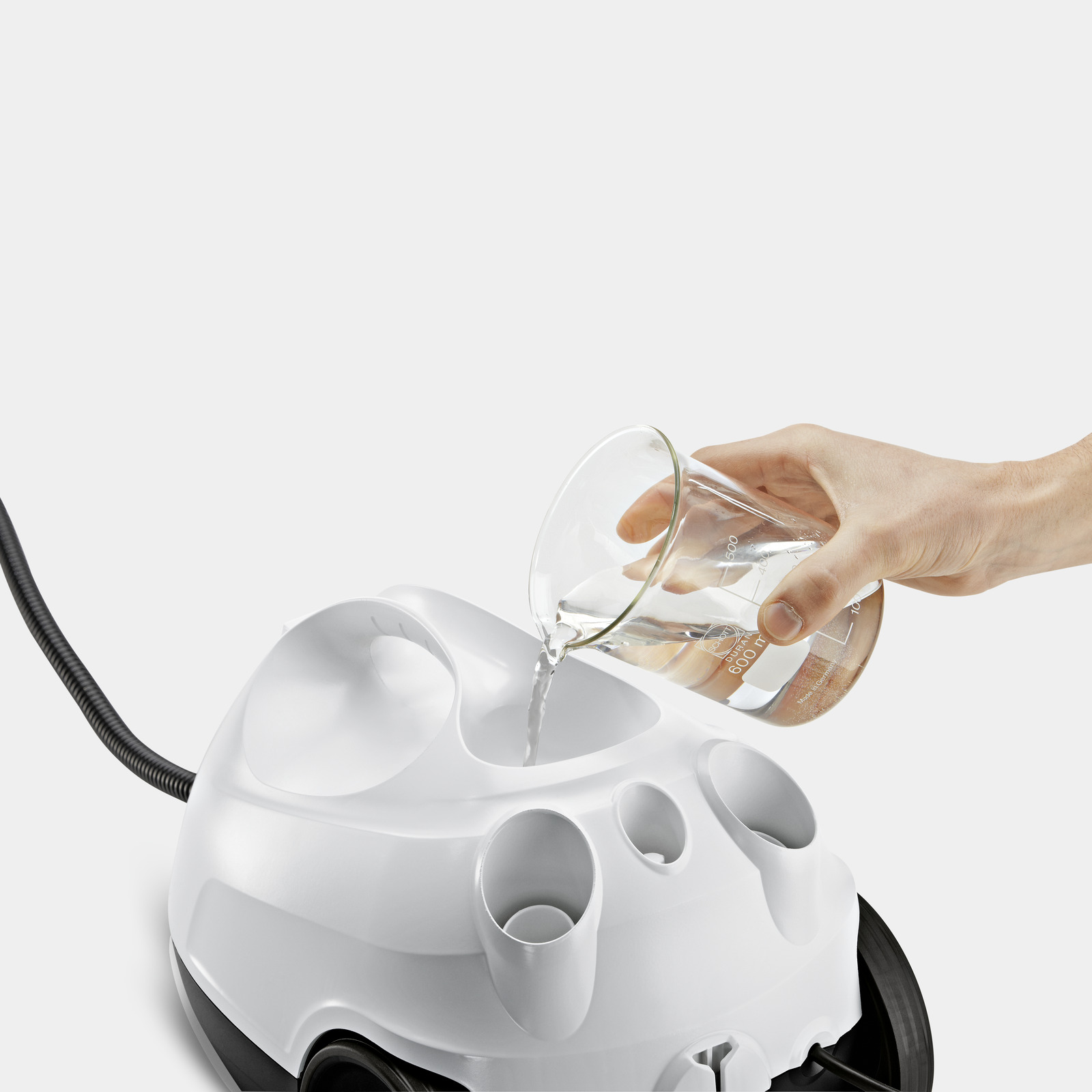 Ręka wlewa wodę z zlewki do białego urządzenia czyszczącego. Tło jest białe.