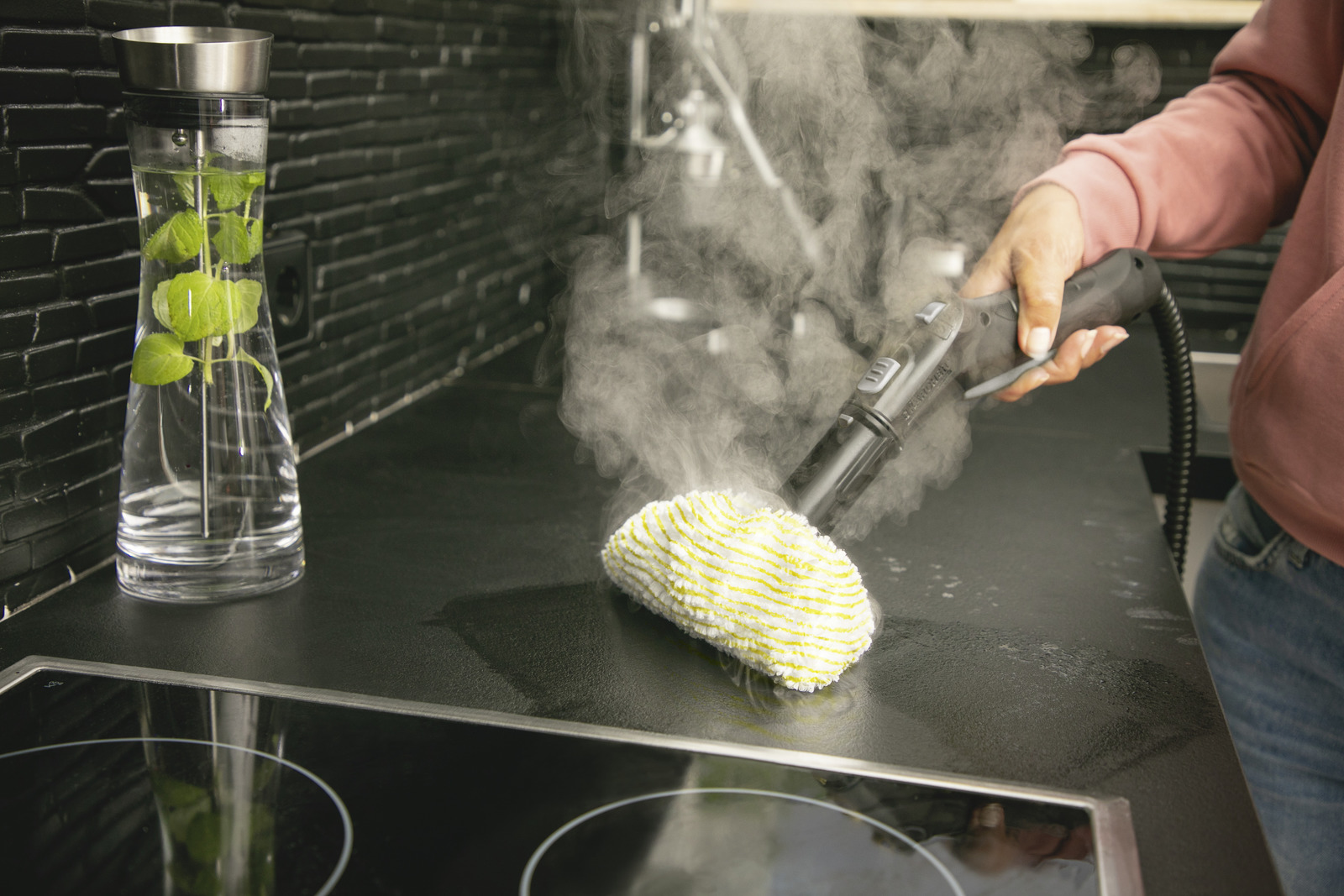 Osoba czyści czarną płytę kuchenną za pomocą parownicy.