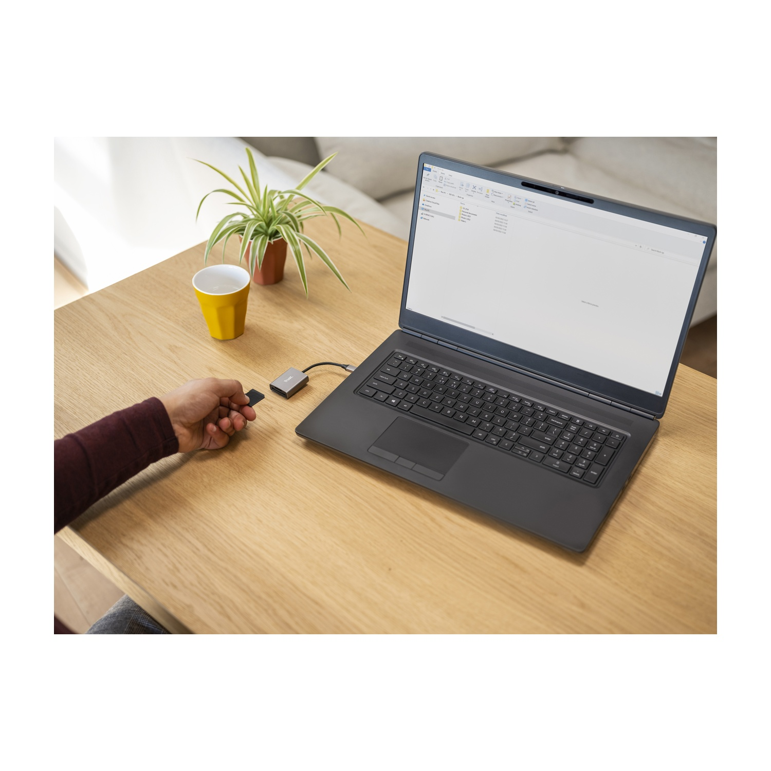 Persona che tiene un lettore di schede accanto a un laptop su un tavolo di legno.