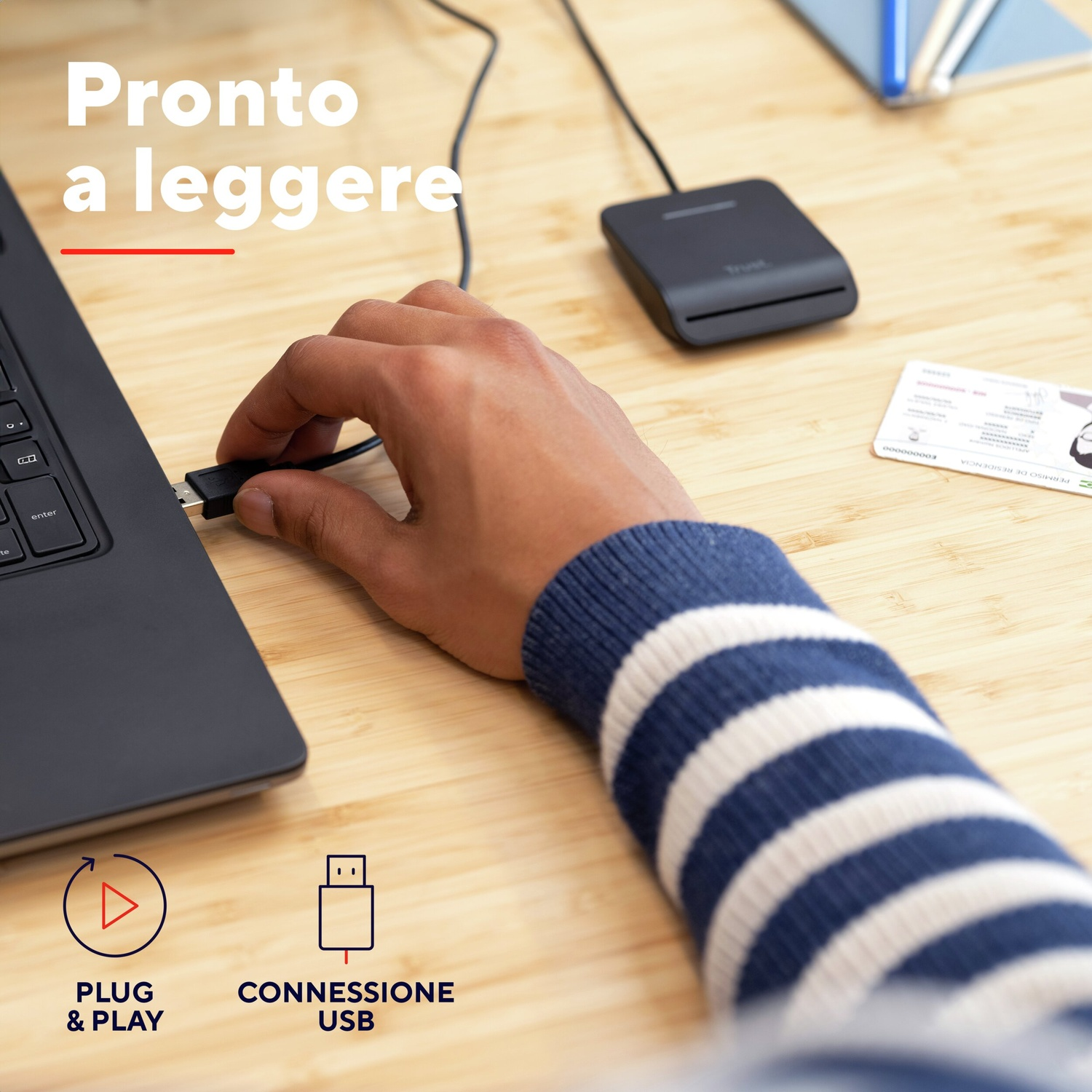 Una mano sta collegando un connettore USB a un laptop. Un lettore di schede e una scheda sono sulla superficie di legno.