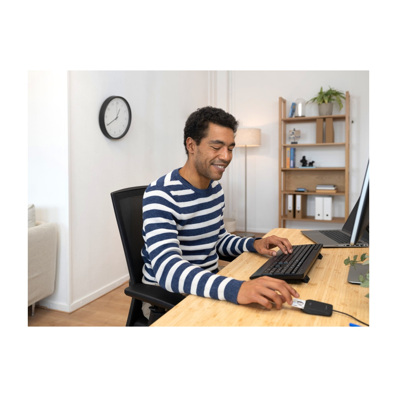 Uomo che usa una tastiera a una scrivania con un computer desktop e un orologio a muro.
