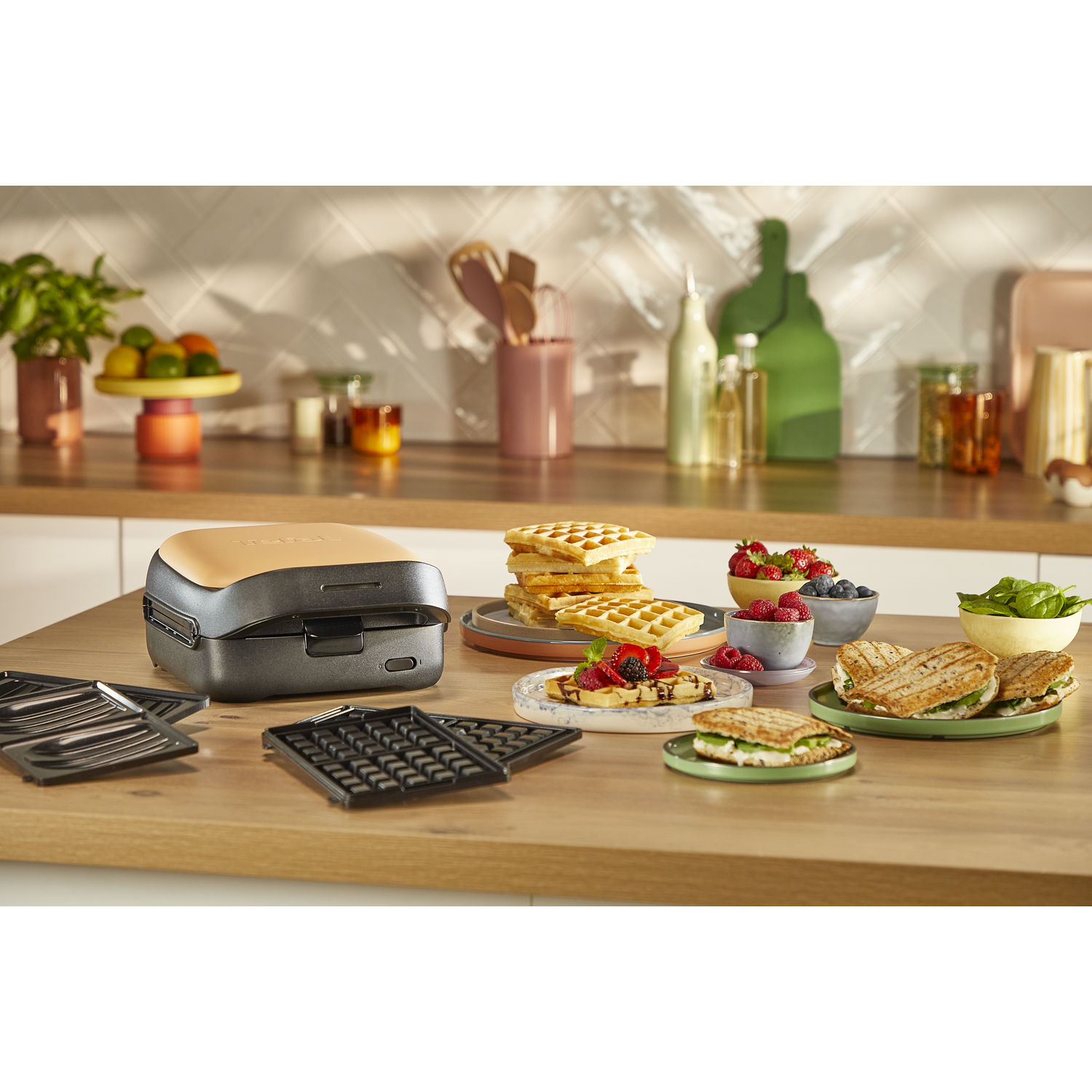 Gaufrier avec gaufres, fruits et sandwichs sur table en bois. Fond de cuisine avec plantes.
