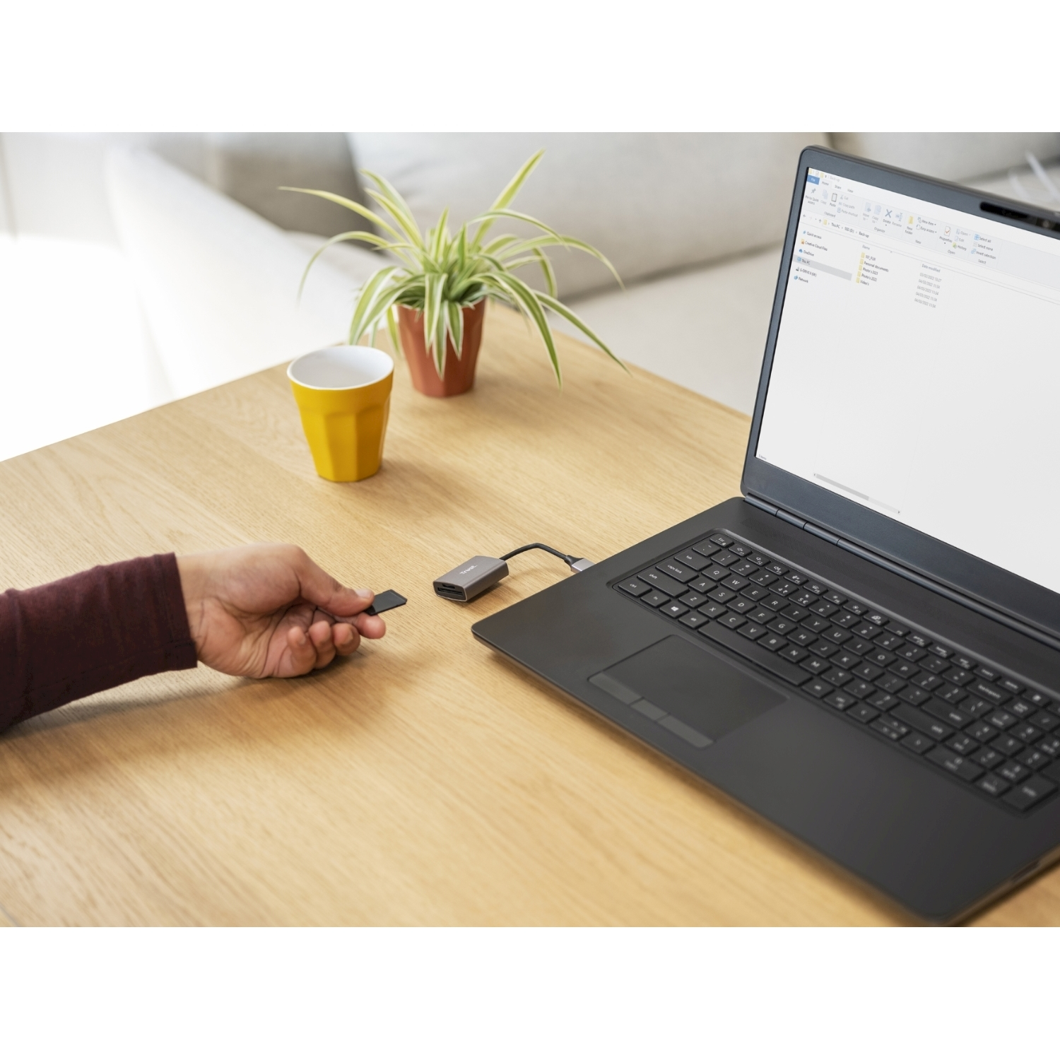 Una persona inserisce una scheda SD in un lettore di schede collegato a un laptop su un tavolo di legno.