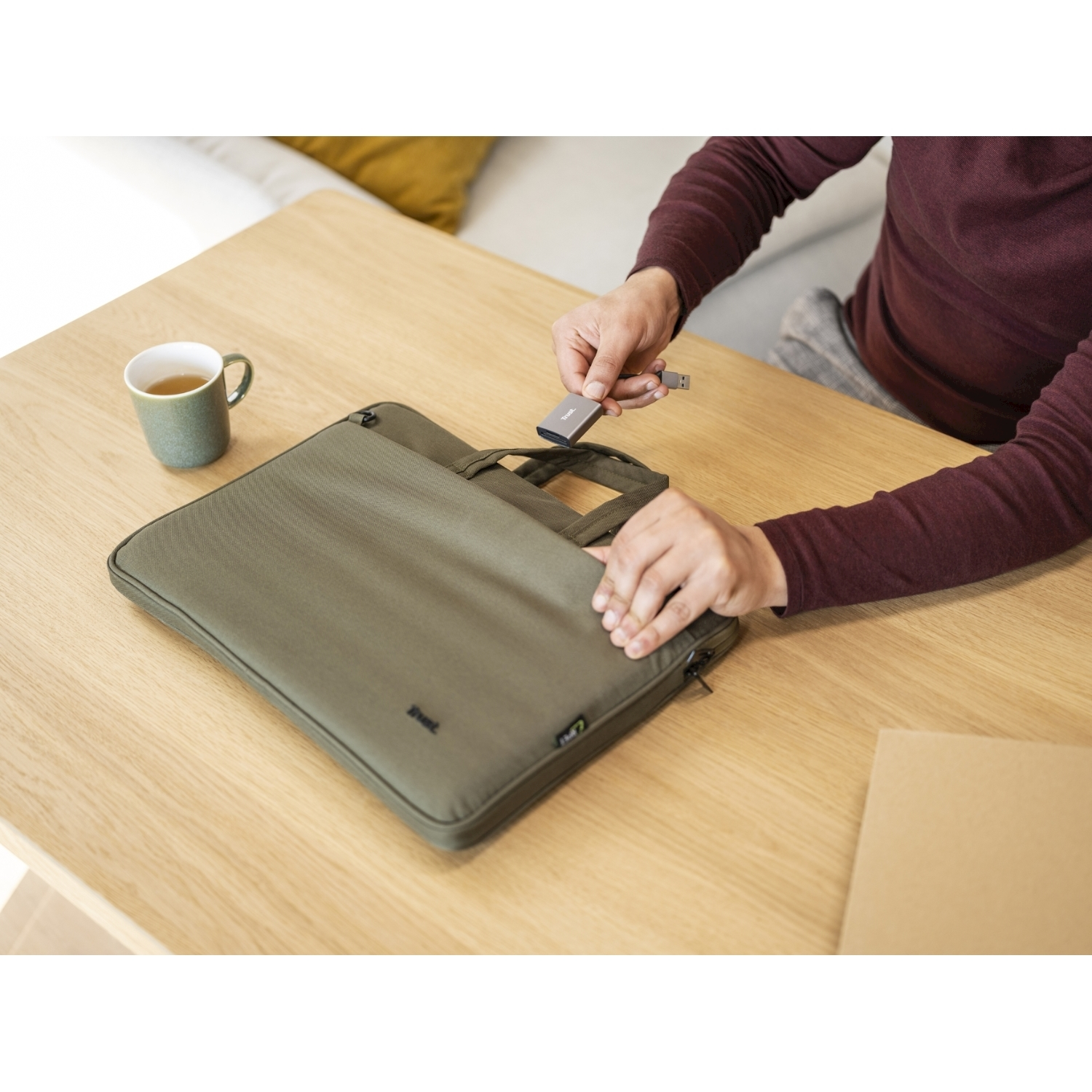 Una persona sta inserendo una chiavetta USB in una custodia per laptop su un tavolo di legno, accanto a una tazza.