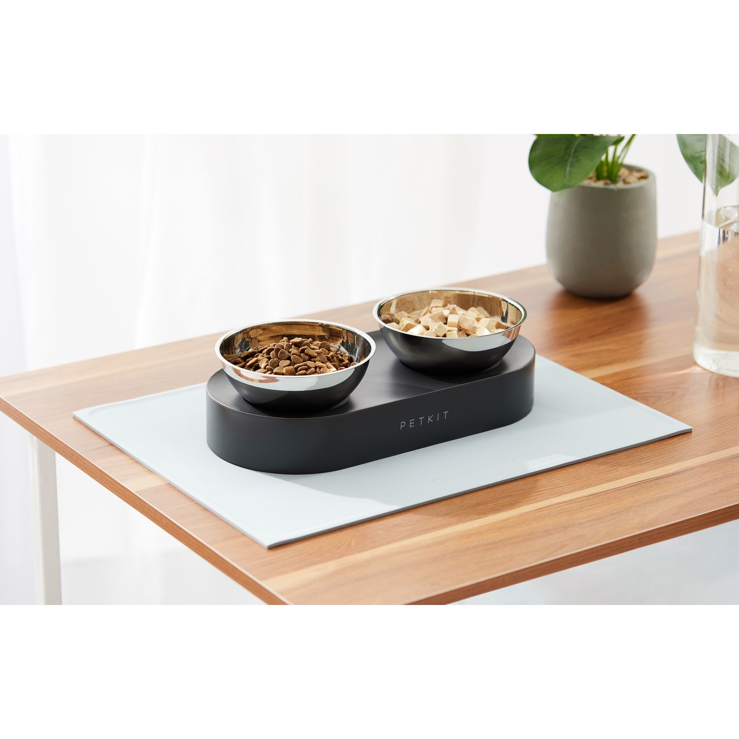 A pet food bowl set on a wooden table. Two silver bowls sit on a black base.