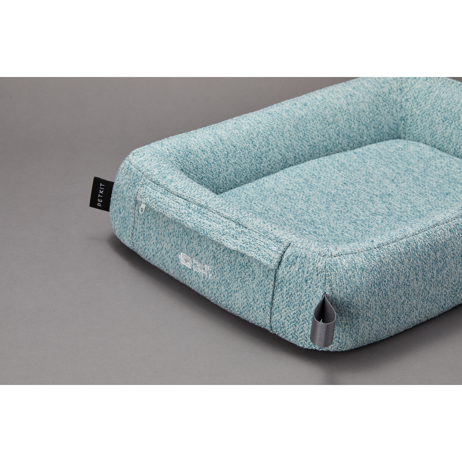 A turquoise pet bed on a gray surface, with a zipper and a PETKIT tag.