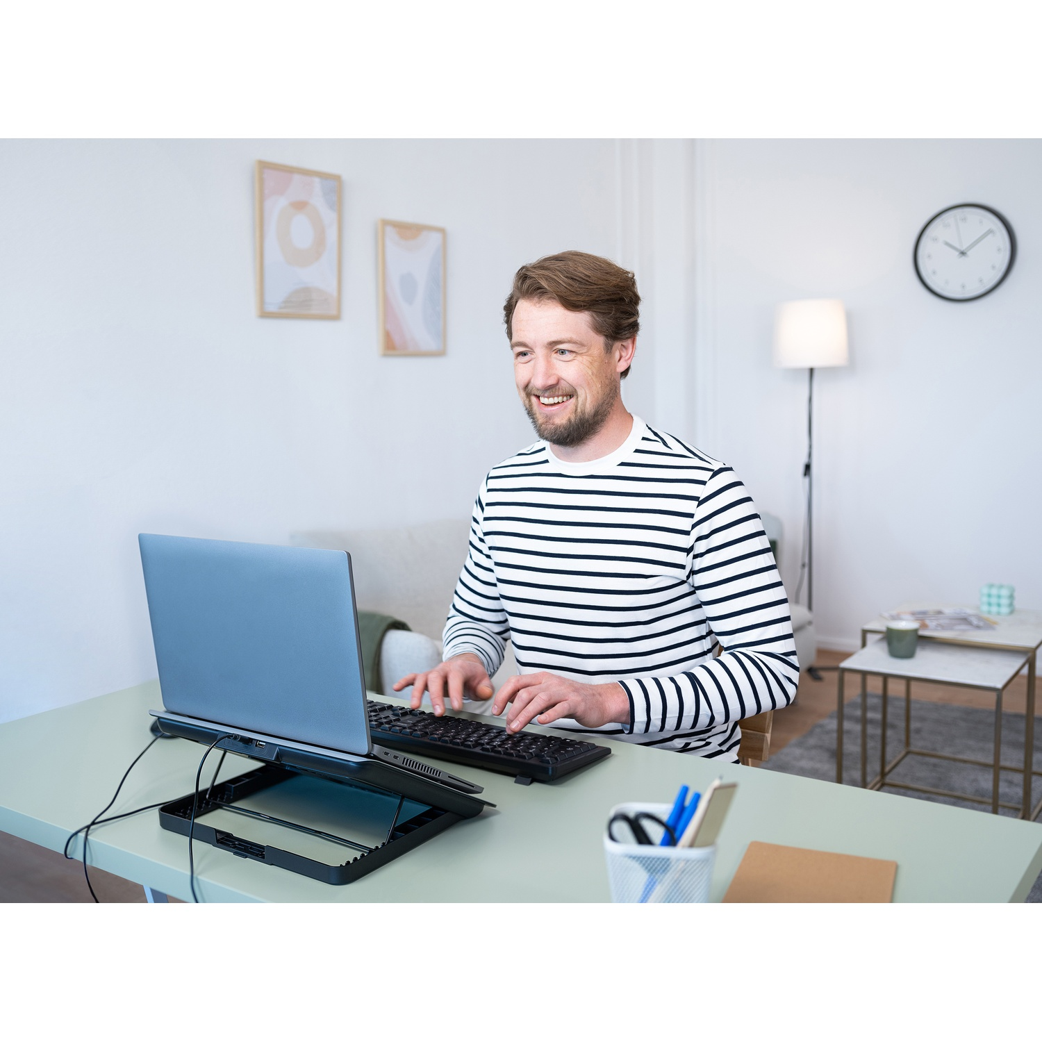 Un uomo sorride mentre digita su una tastiera collegata a un laptop su una scrivania. Ci sono disegni sul muro.