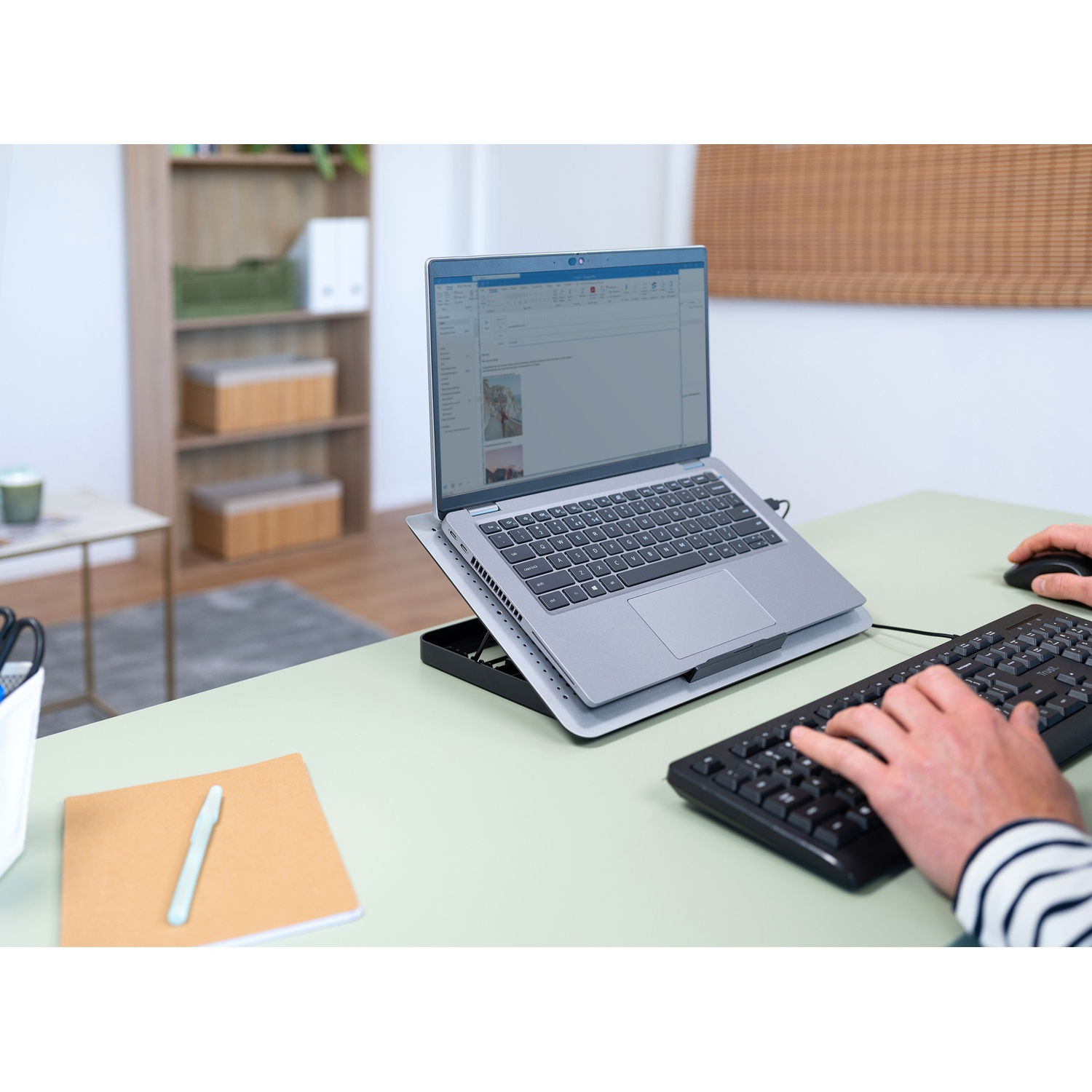 Un laptop su una scrivania con tastiera e mouse. Lo schermo mostra un documento. Le mani di una persona sulla tastiera.