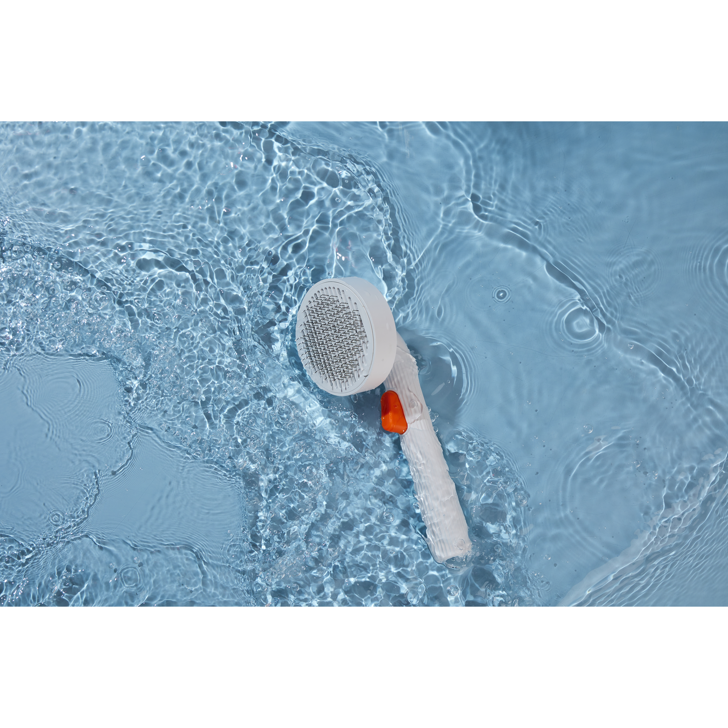 A white and orange shower head is held in blue water with ripples.