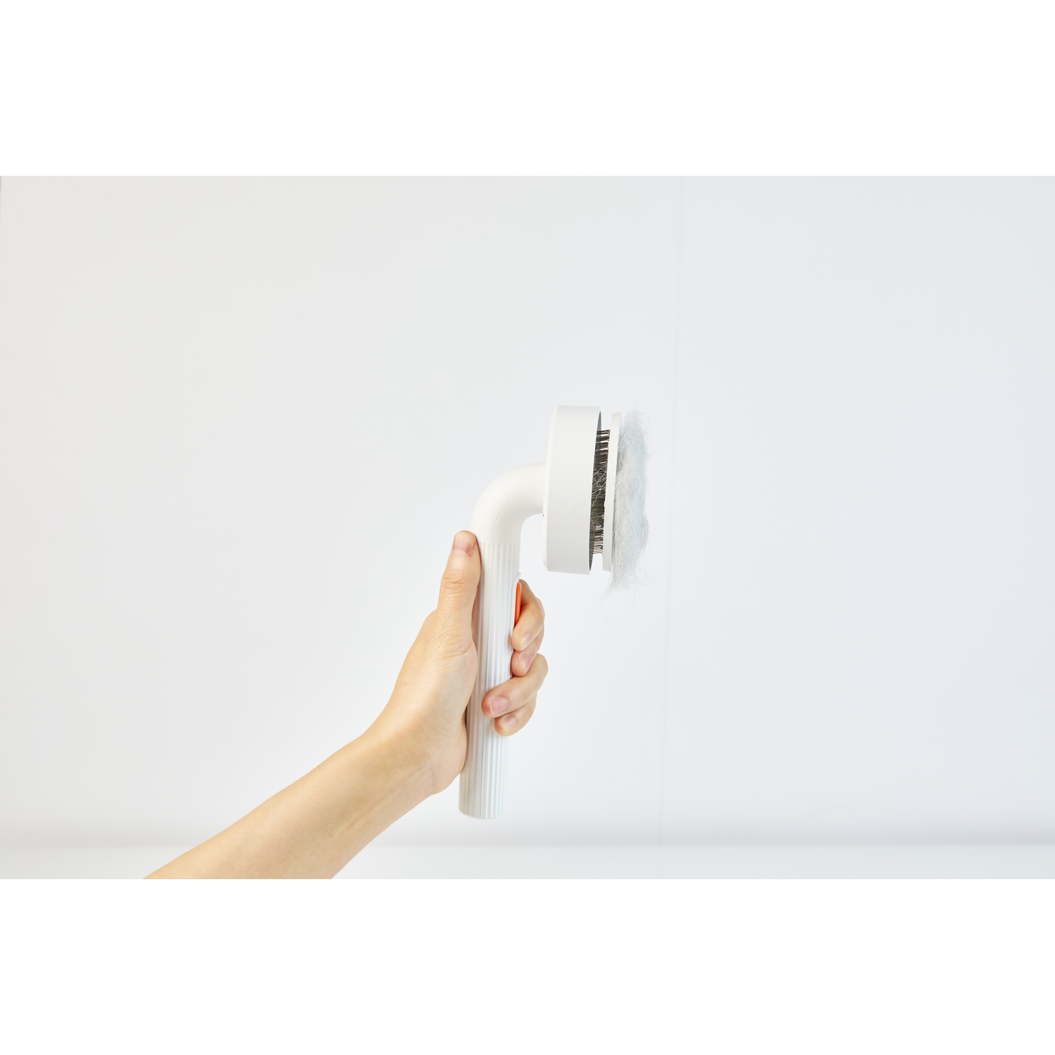 A hand holding a white and orange pet brush with hair on the brush.