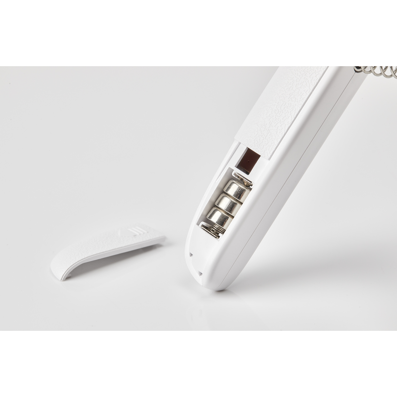 A white remote control with an open battery compartment exposing three batteries.