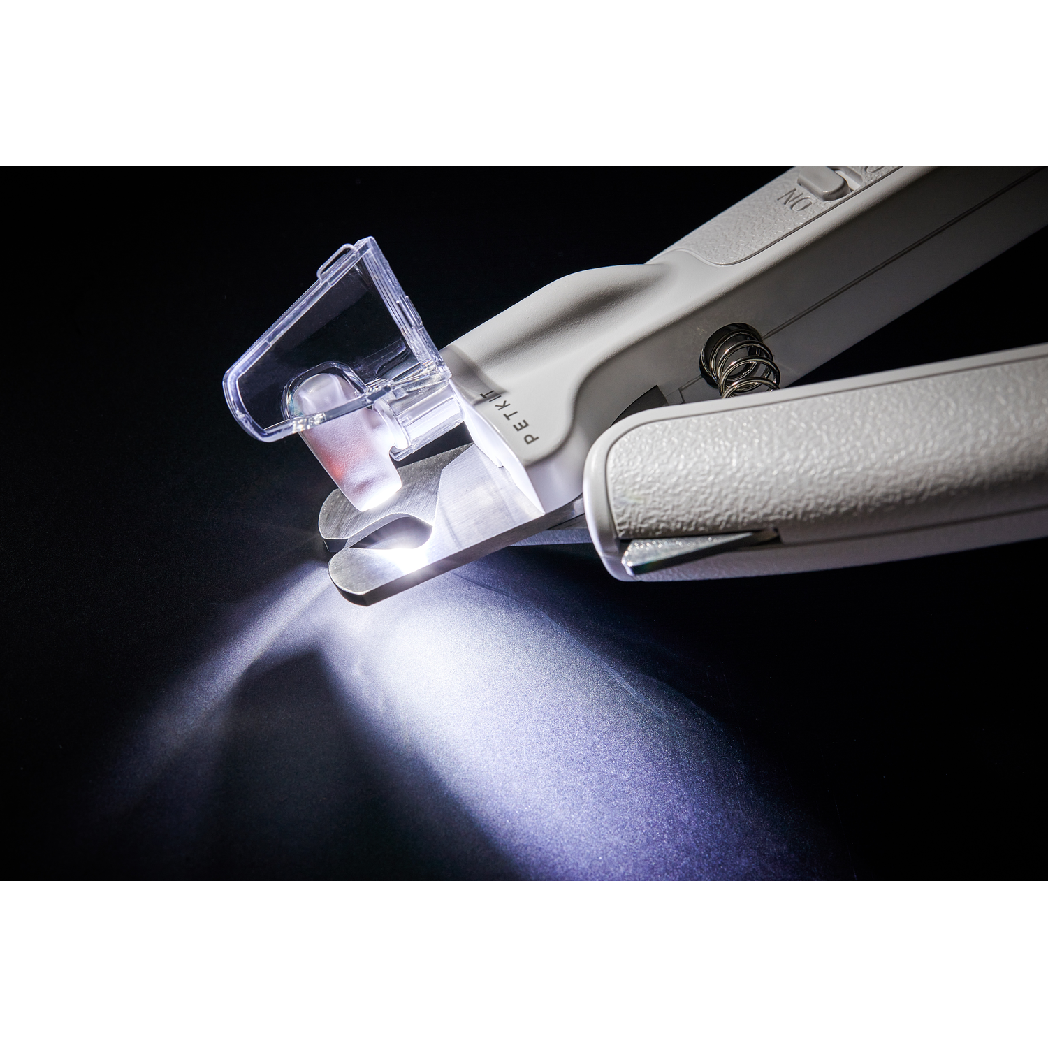 Pet nail clippers. The clippers are white. The light is on. The background is black.