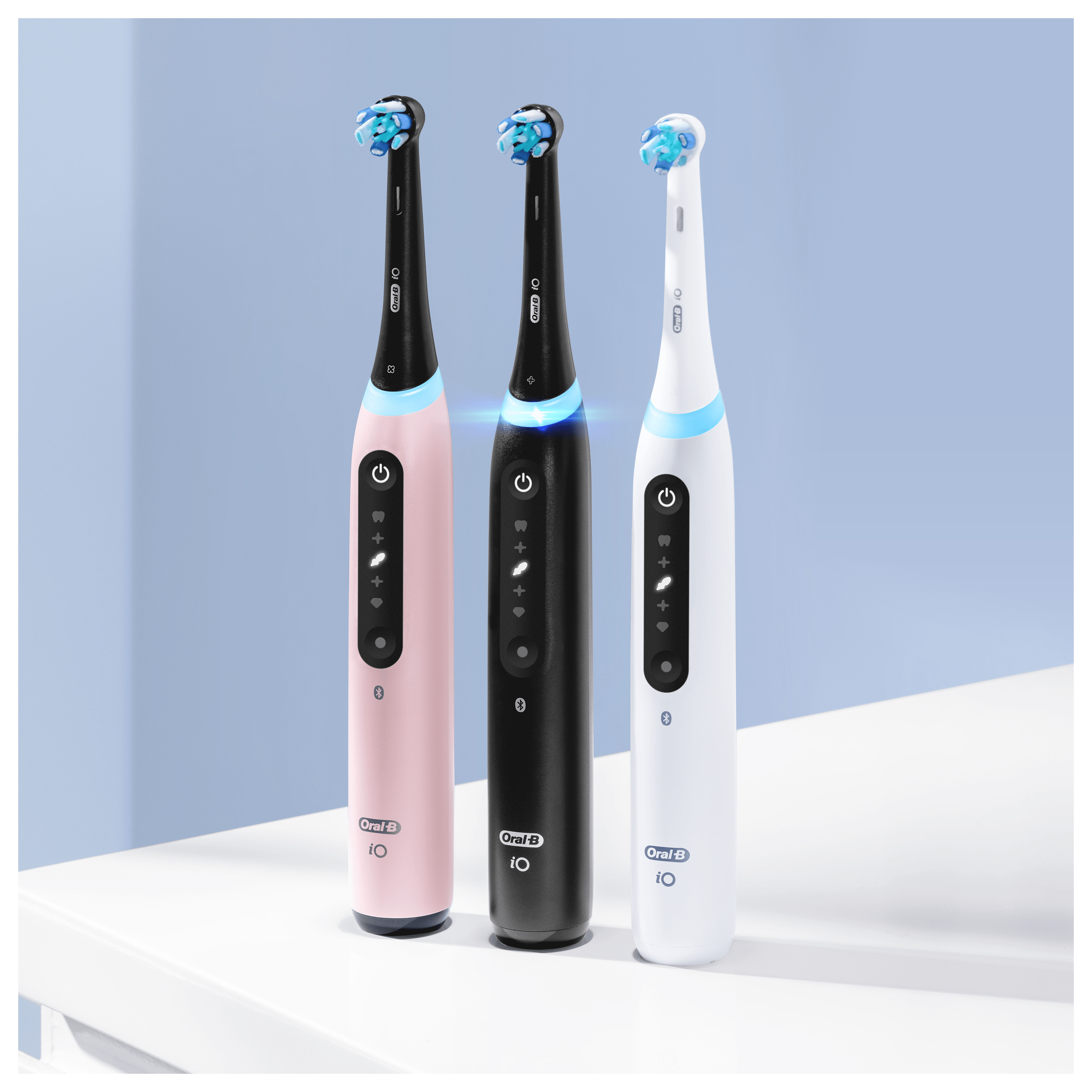Tres cepillos de dientes eléctricos en rosa, negro y blanco. Se encuentran de pie sobre una superficie blanca contra un fondo azul.