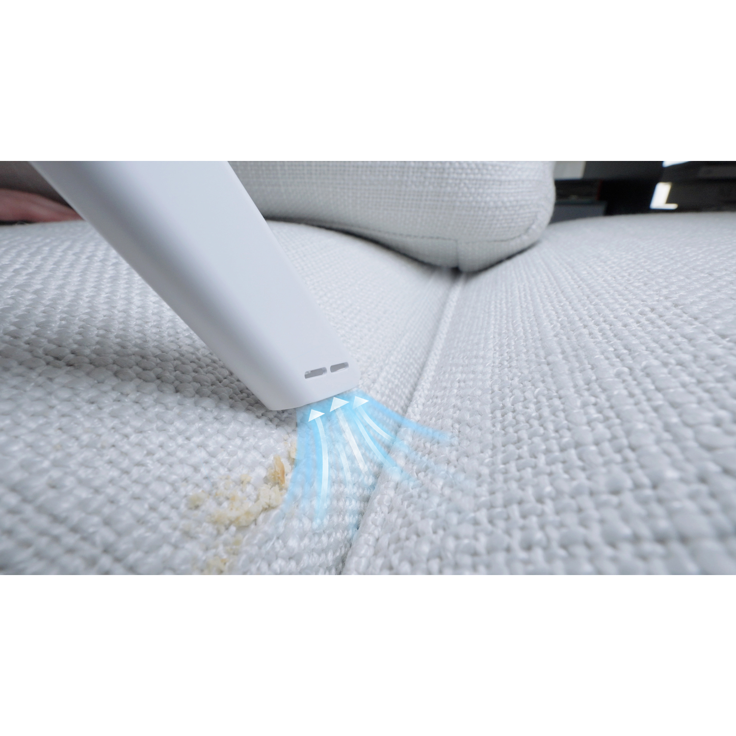 A white handheld vacuum cleaner cleaning a light-colored sofa, removing stains.