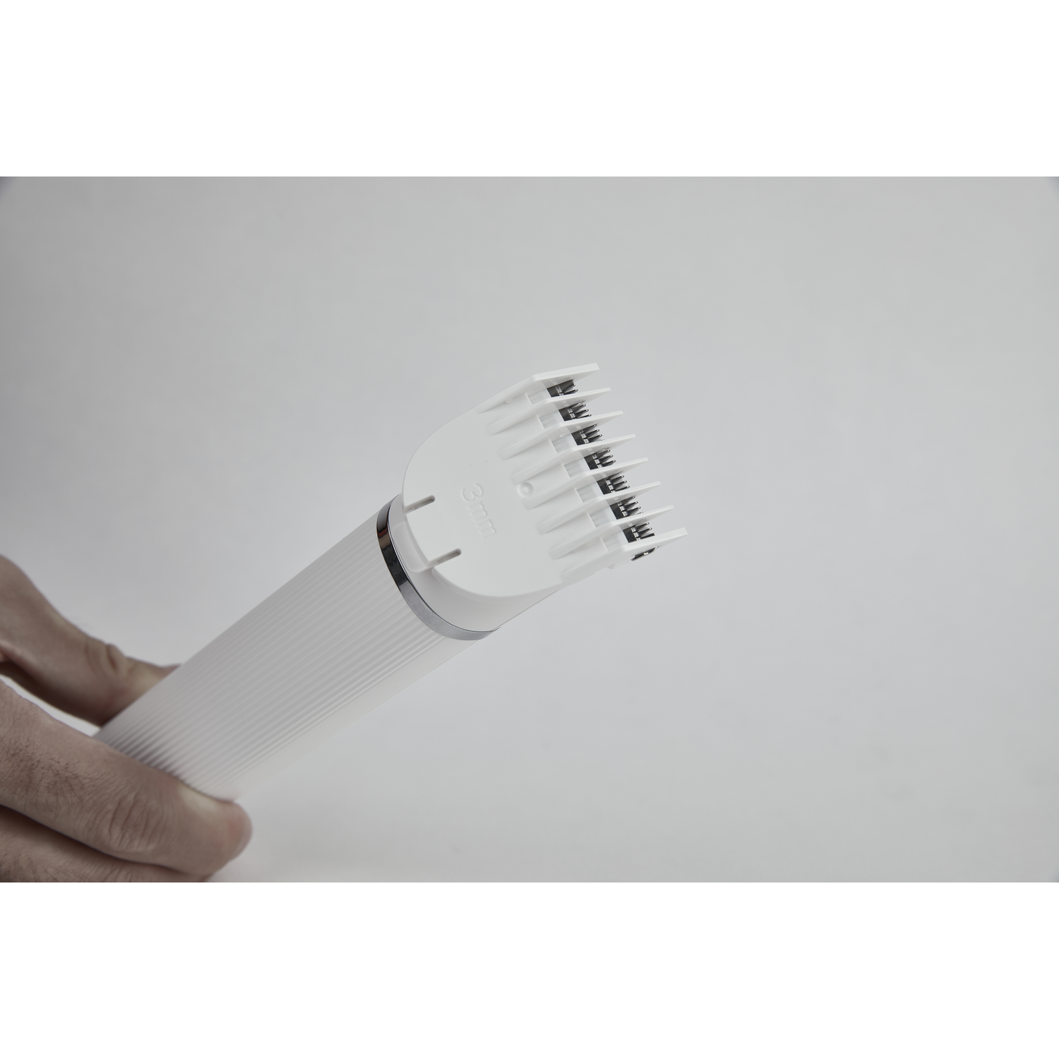 A white electric hair trimmer with a cutting attachment, held by a person.