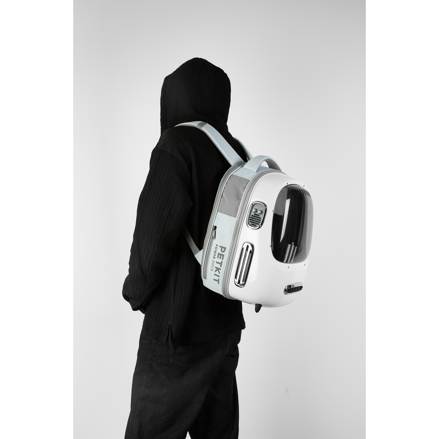 Person wearing a black hooded jacket with a white pet carrier backpack.