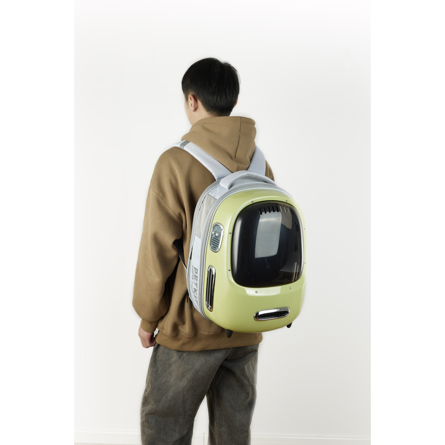 Man in brown hoodie with a green cat backpack. White background.