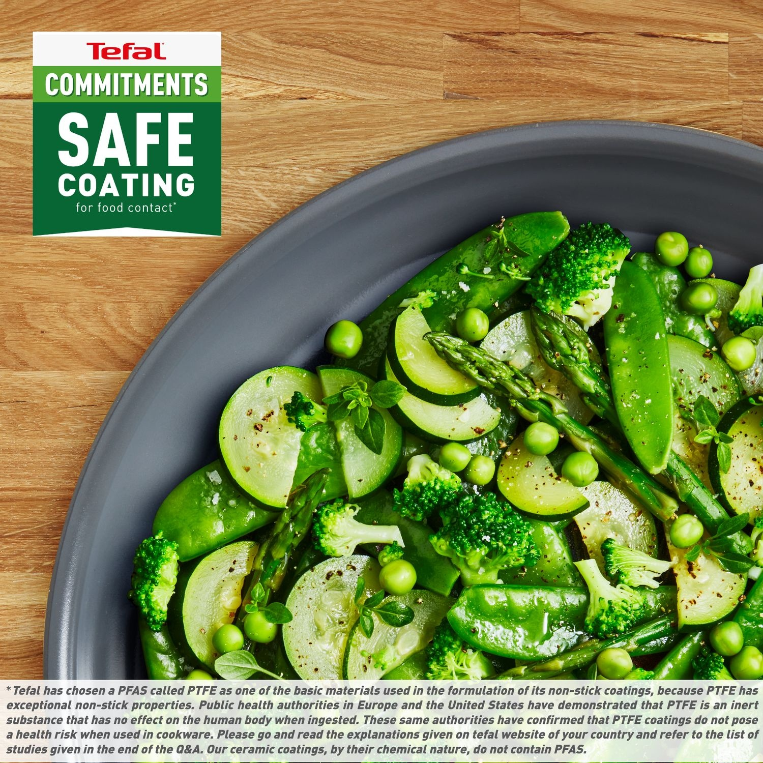 A plate of green vegetables on a wooden table. Includes zucchini, peas, broccoli, and asparagus. A Tefal safe coating logo is visible.