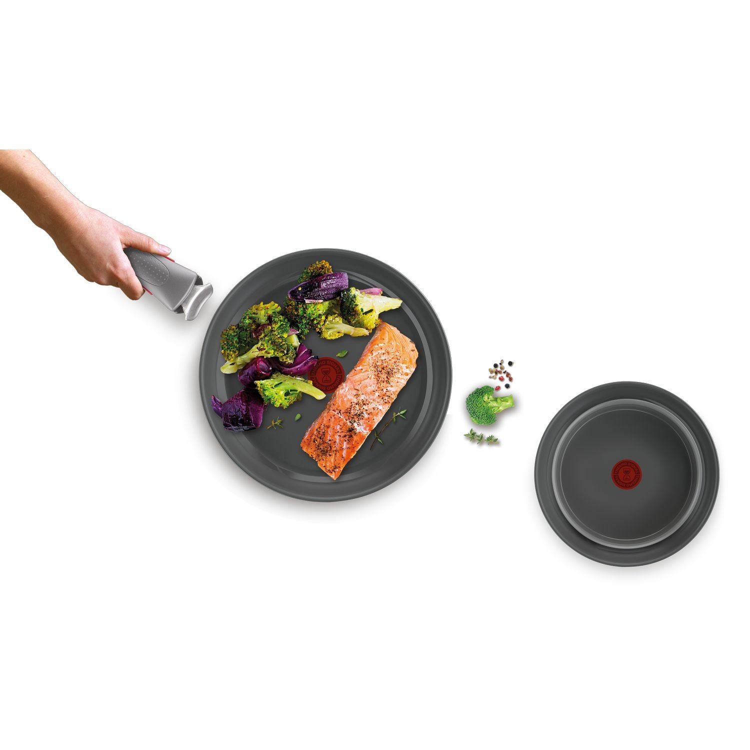 Bord met zalm, broccoli en groenten. Hand houdt panhendel vast. Ander bord ernaast.