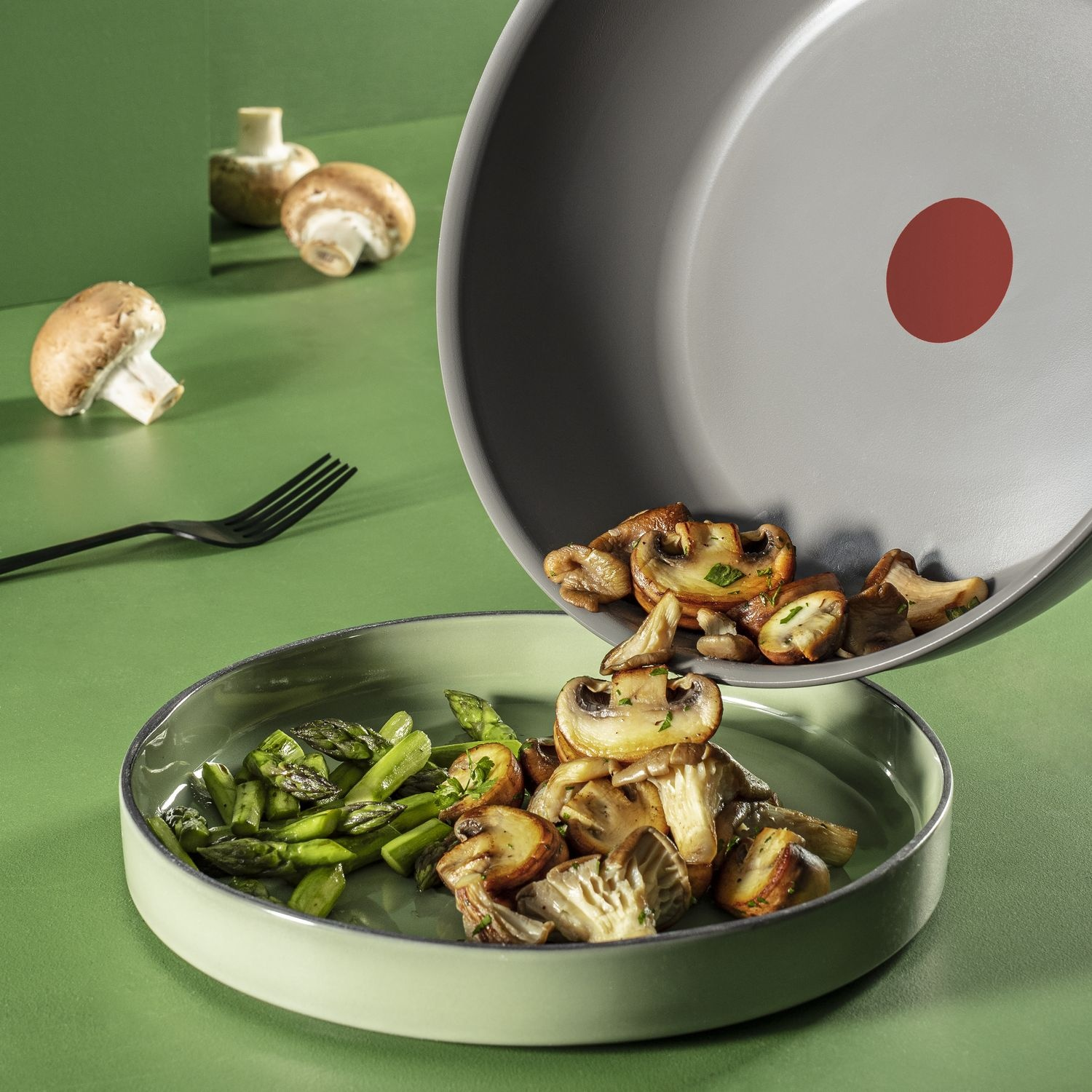 Des champignons et des asperges sont versés d'une poêle dans une assiette.