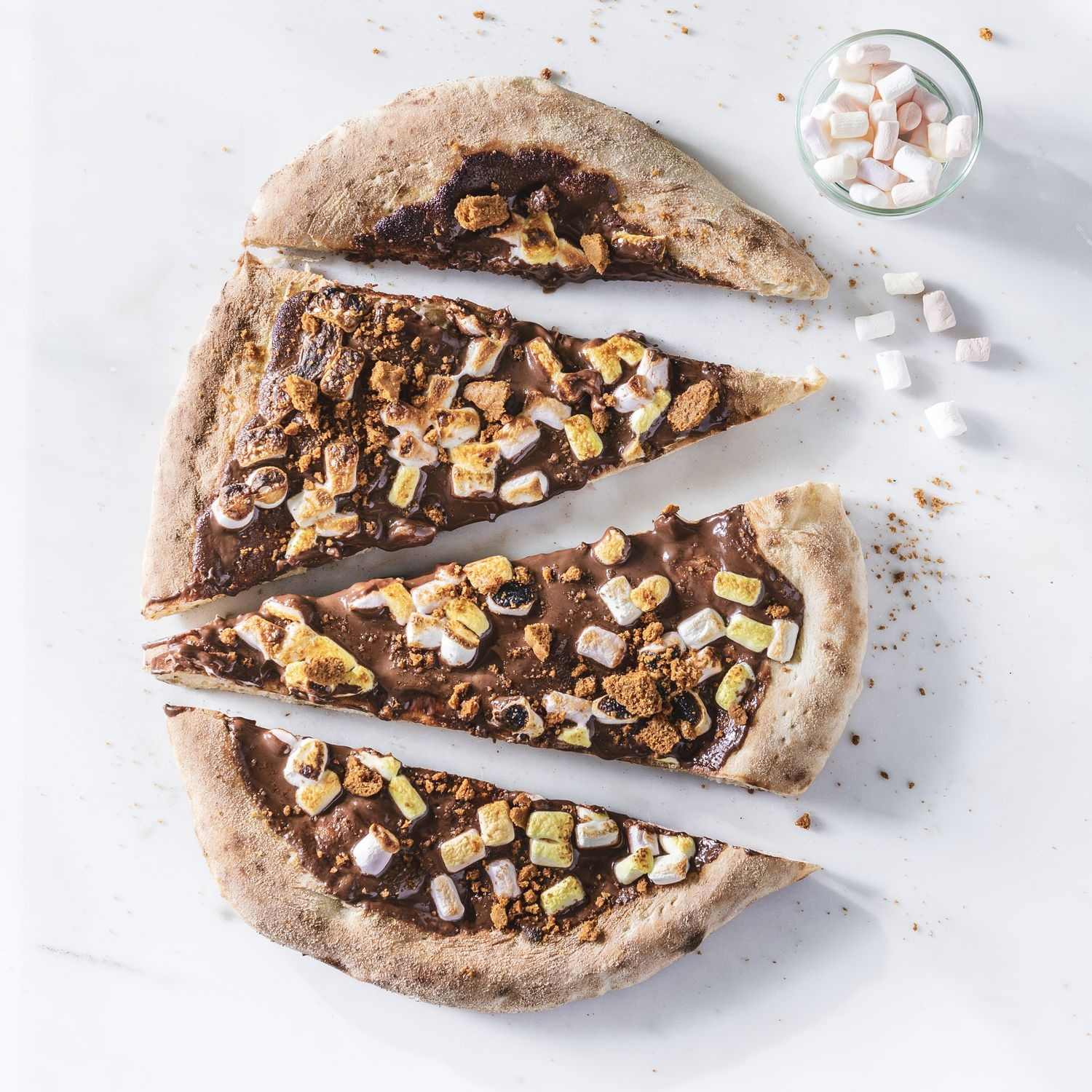 Quatre tranches de pizza au chocolat avec des guimauves et des biscuits émiettés.