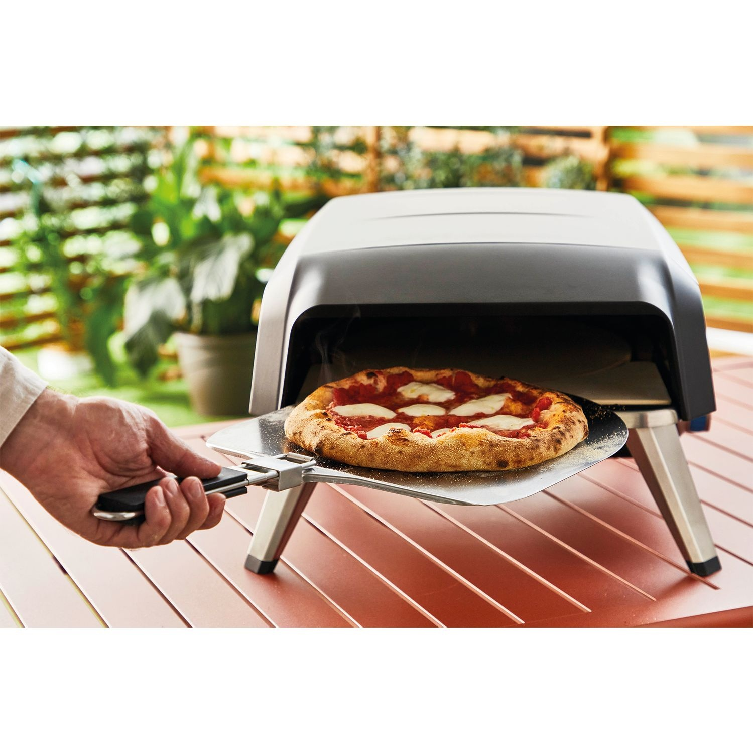 Une personne retire une pizza d'un four noir avec une pelle en métal sur une table.
