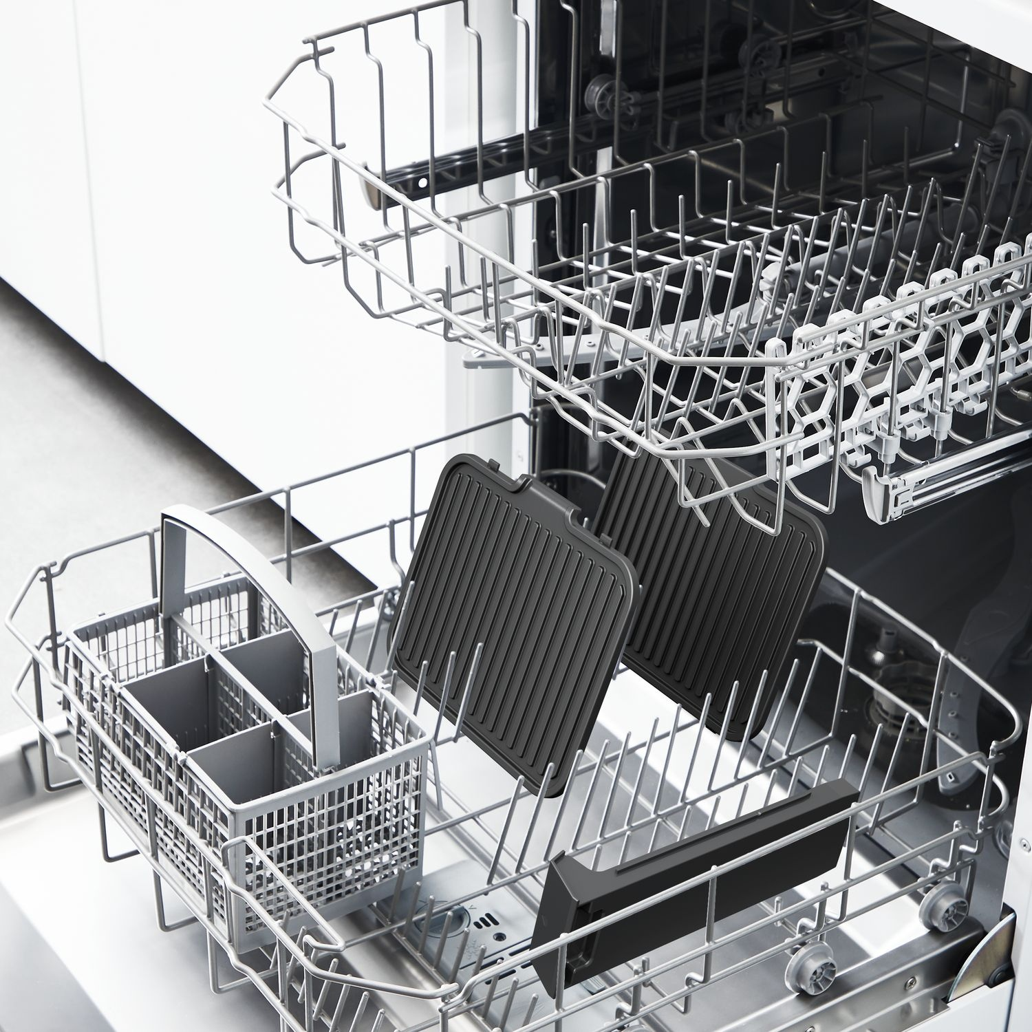 Dishwasher with two black grill plates, a utensil basket, and metal racks inside a white kitchen.
