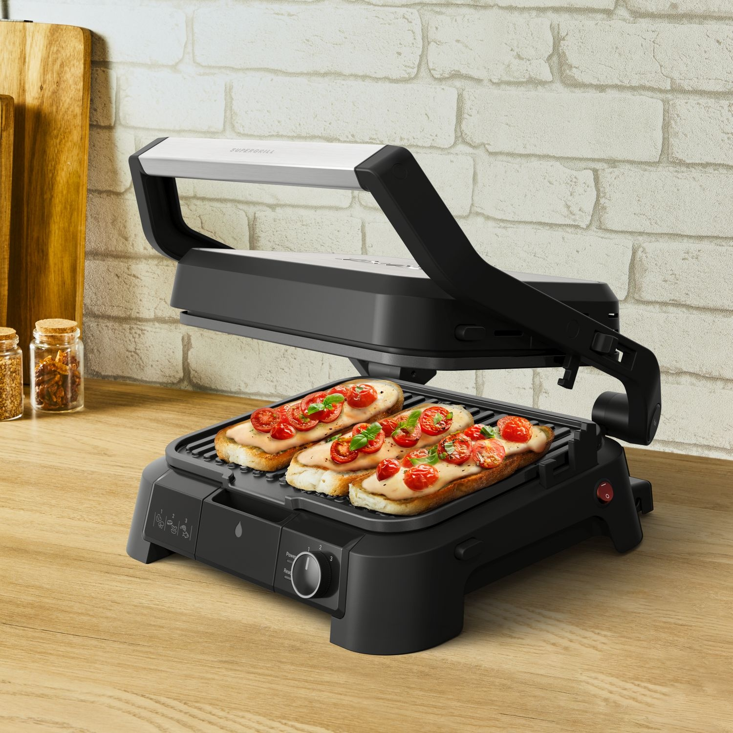 A black panini press with toasted sandwiches topped with tomatoes on a wooden surface.