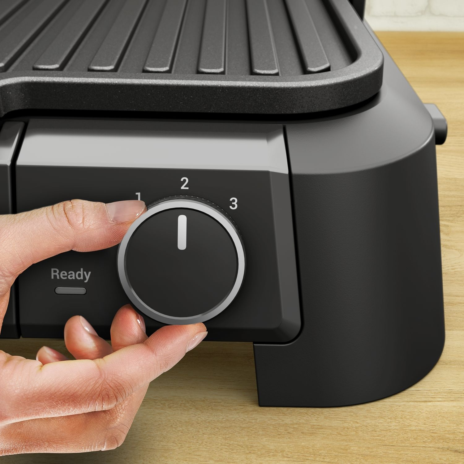 Close-up of a person's hand turning a black dial on a black grill, numbers 1, 2, and 3 are visible.